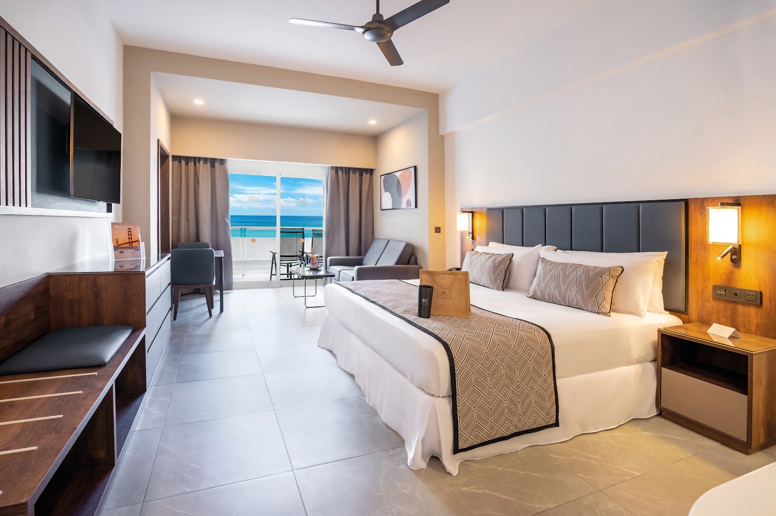 Spacious resort bedroom with king bed, ocean view balcony, sitting area, and flat-screen TV overlooking turquoise Caribbean waters.