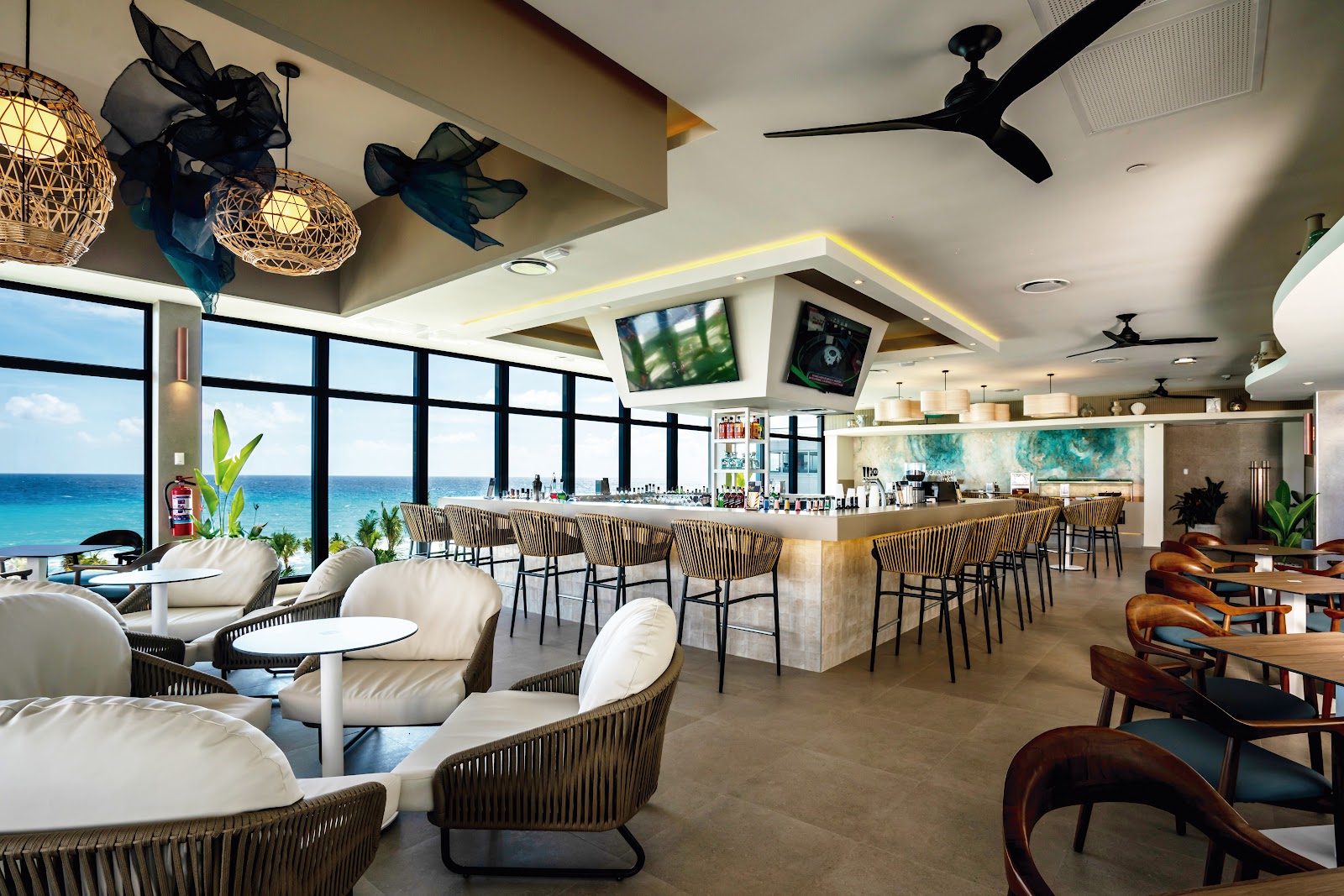 Indoor pool area at Riu Palace Kukulkan with blue lap pools, lounge chairs, modern ceiling with skylight, and tropical vegetation visible through floor-to-ceiling windows.