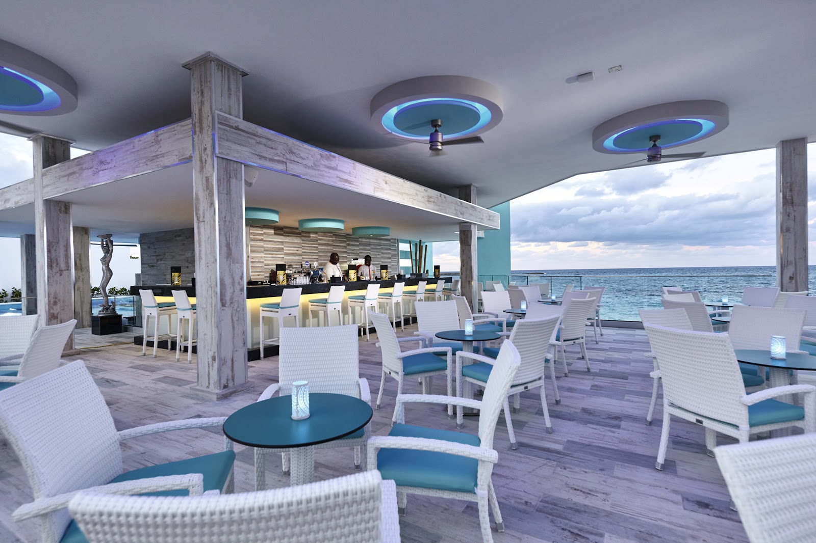 White lounge chairs with blue cushions on a covered oceanfront terrace with bar and ocean view at Hotel Riu Palace Paradise Island.