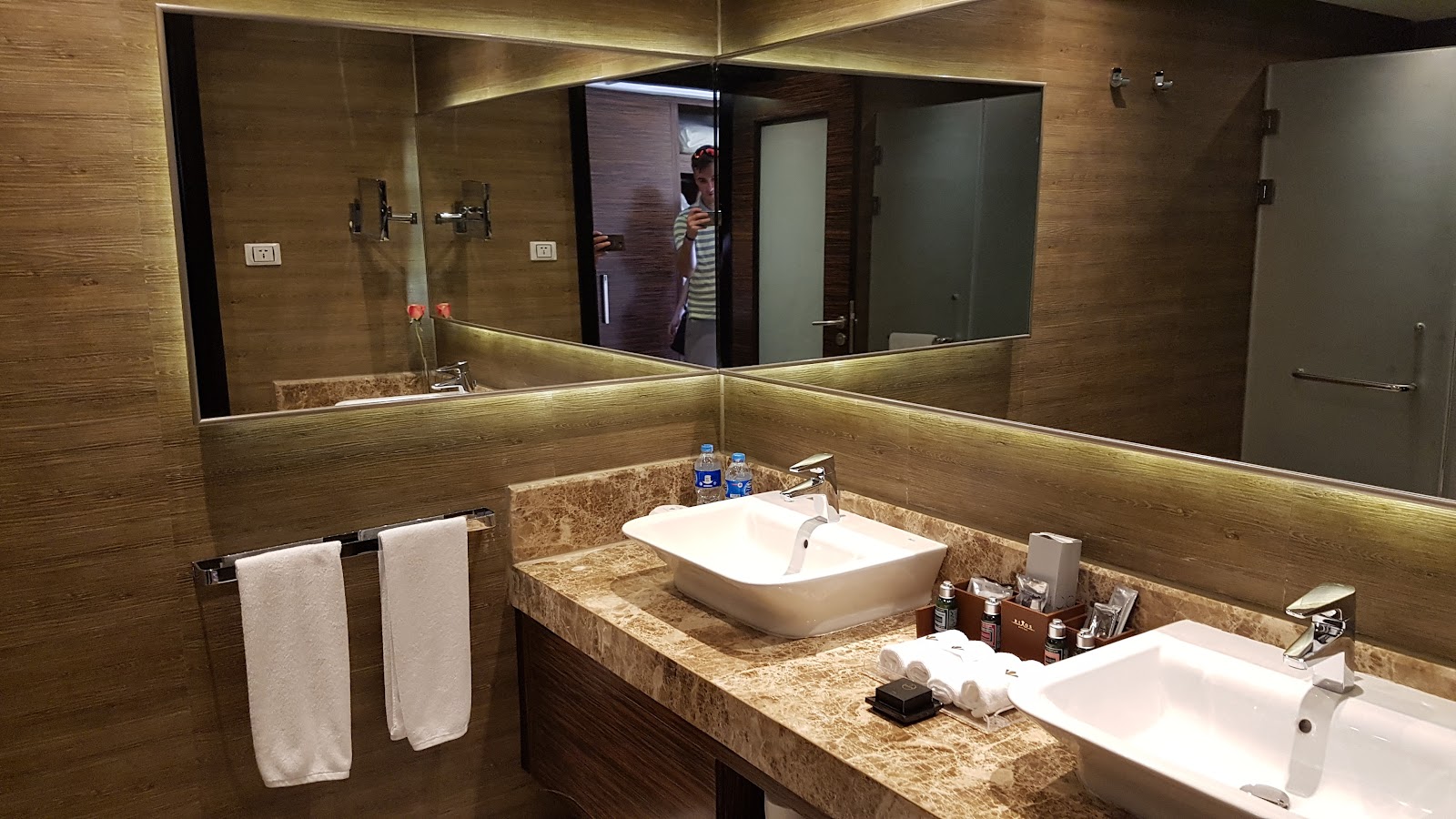 Bathroom with dual vessel sinks, lit mirrors, and wood-textured walls at Rixos Premium Seagate.