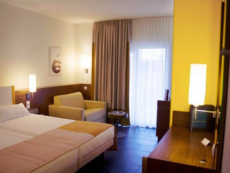 Resort guest room with queen bed, yellow armchair, and balcony access at Robinson Quinta da Ria.