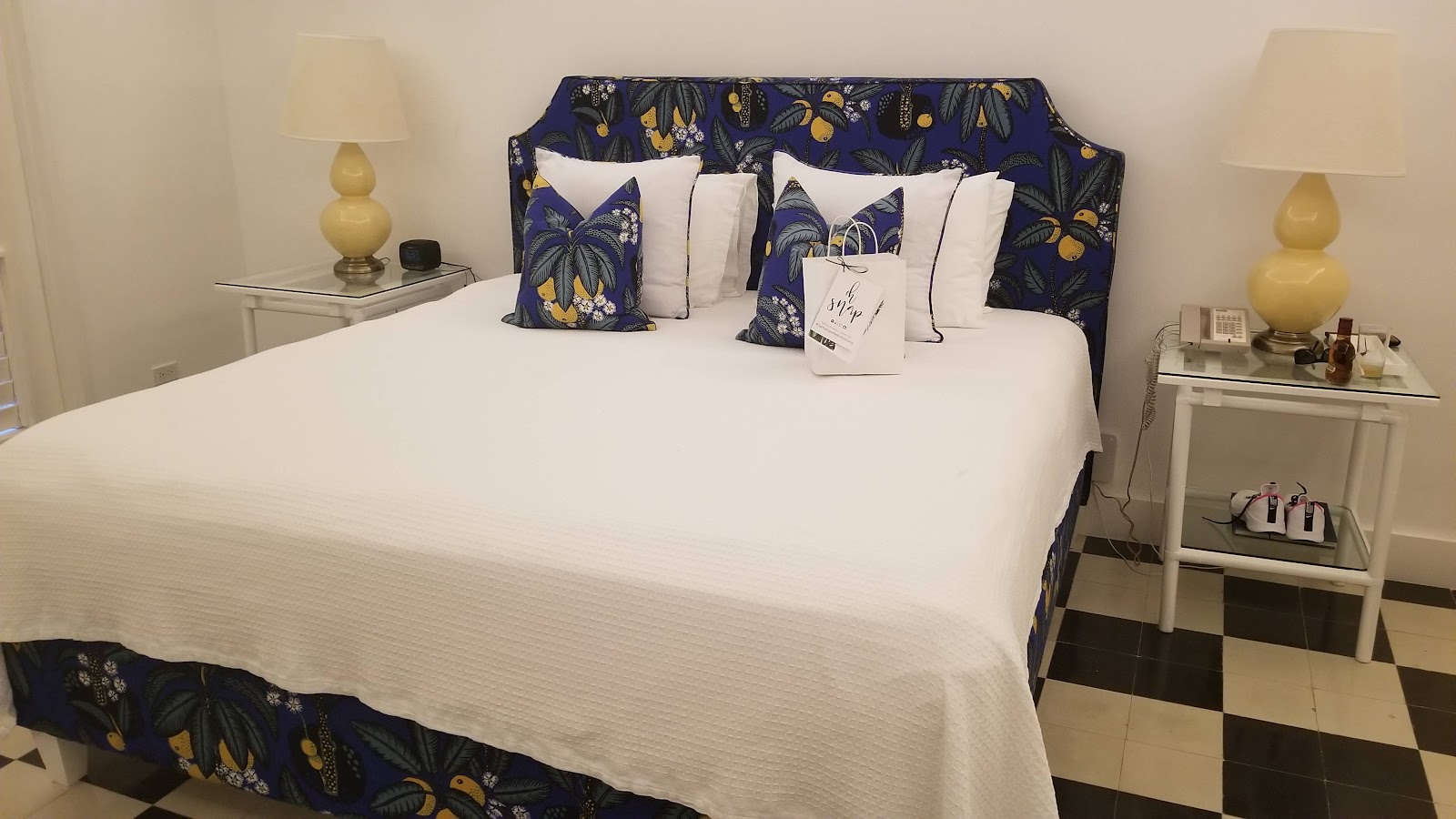 King bed with blue floral headboard and coordinating pillows, white bedding, yellow table lamps, and checkered flooring in a resort guest room.