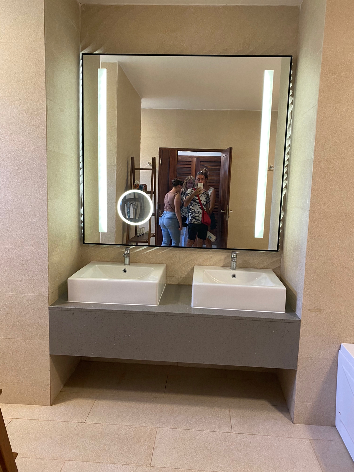 Bathroom vanity with two white square sinks, illuminated mirror, and beige tile walls at Royal Zanzibar Beach Resort.