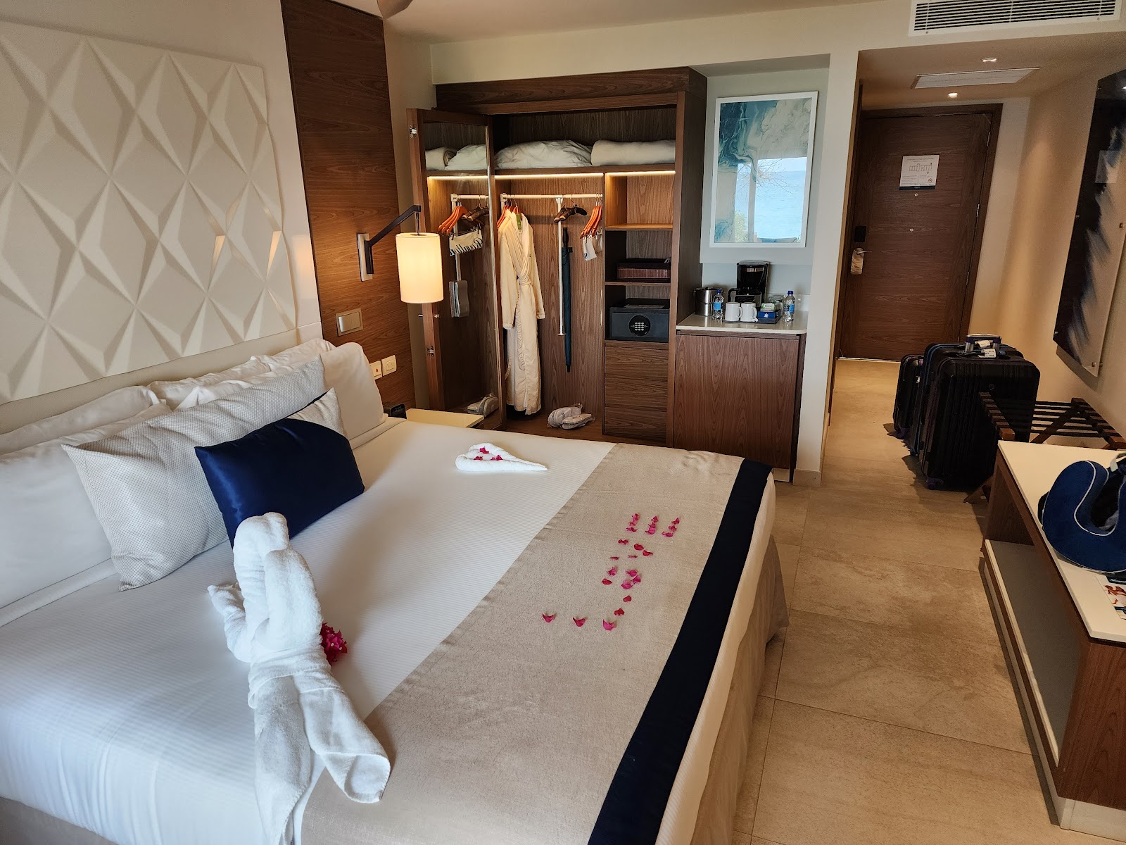 Spacious resort bedroom with two queen beds dressed in white linens with navy accents, modern geometric wall panels, and a balcony overlooking palm trees.