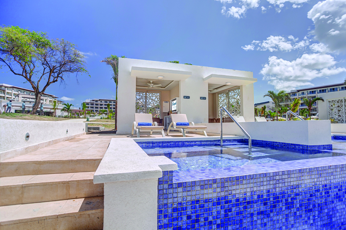 Blue-tiled pool with loungers and white cabanas at Royalton Saint Lucia, resort buildings visible beyond under clear sky.