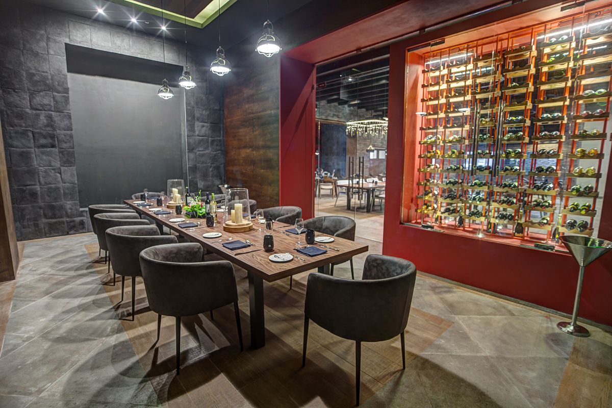 Private dining room at Royalton Saint Lucia with wooden table, gray upholstered chairs, pendant lights, and red wine wall display.