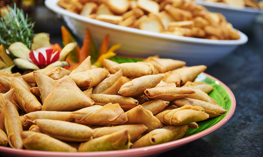Fried spring rolls arranged on a pink plate with carved vegetable garnish and bowls of appetizers in the background.