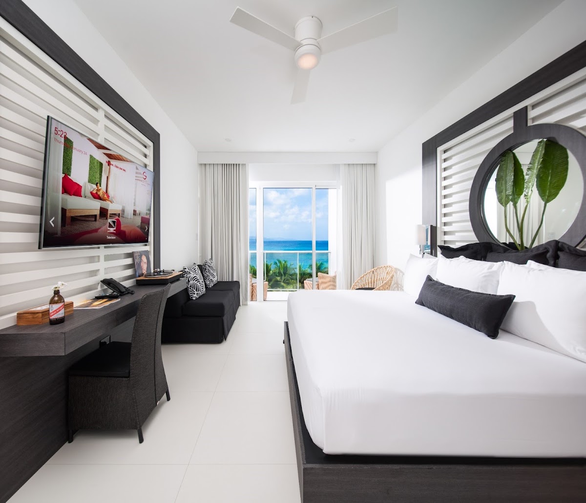 Modern resort guestroom with white bed, dark wood desk, and ocean view through balcony doors at S Hotel Montego Bay.