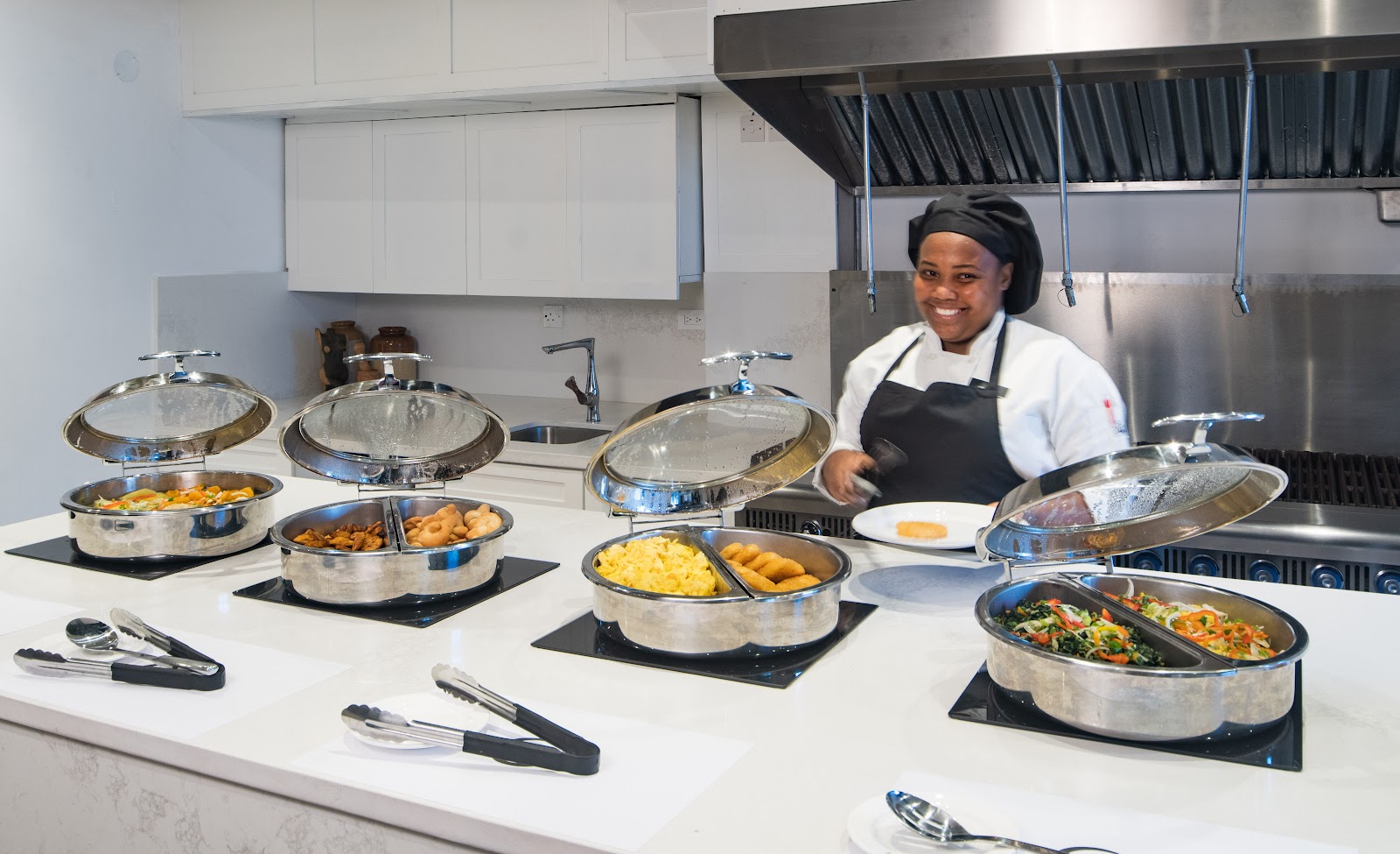 Indoor buffet dining area with fruit display, warming trays, and wooden counters at S Hotel Montego Bay.