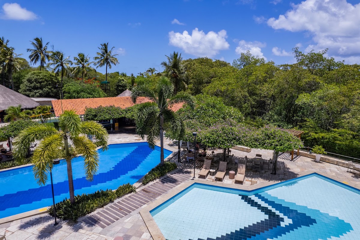 Two blue pools with geometric tile patterns sit in front of a terracotta-roofed building at Salinas Maragogi, surrounded by palm trees and tropical vegetation.