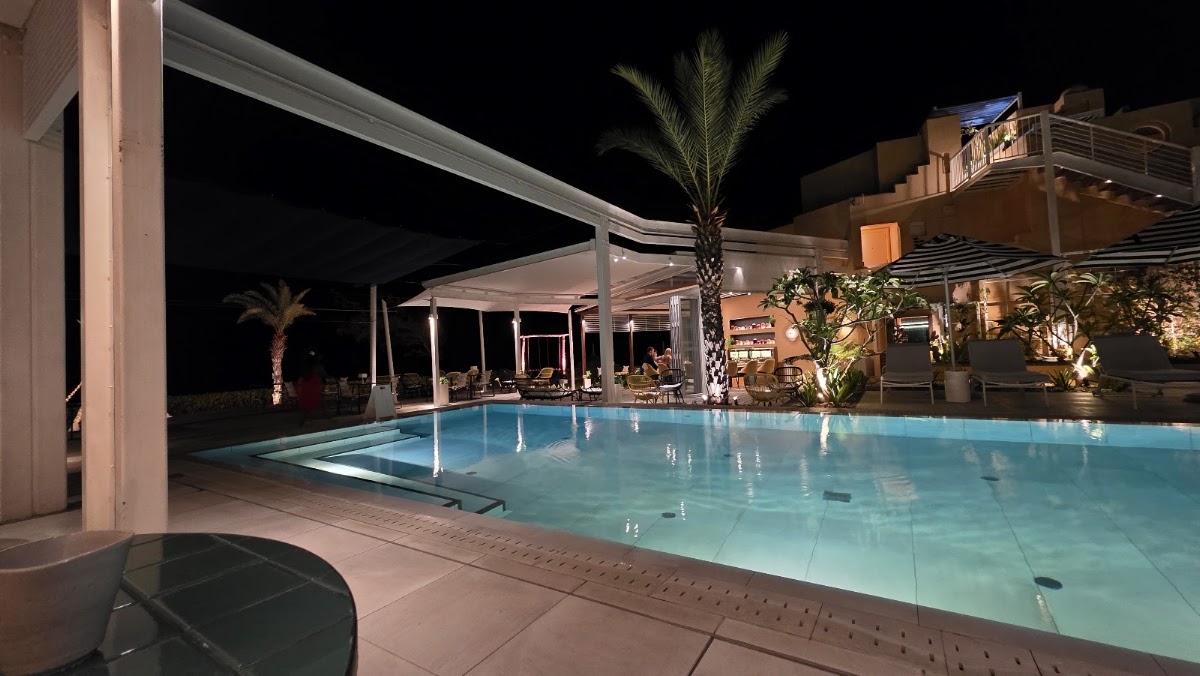 Illuminated swimming pool at night with white pergola structures, palm trees, and tan-colored resort buildings surrounding the terrace at SALT of Palmar.