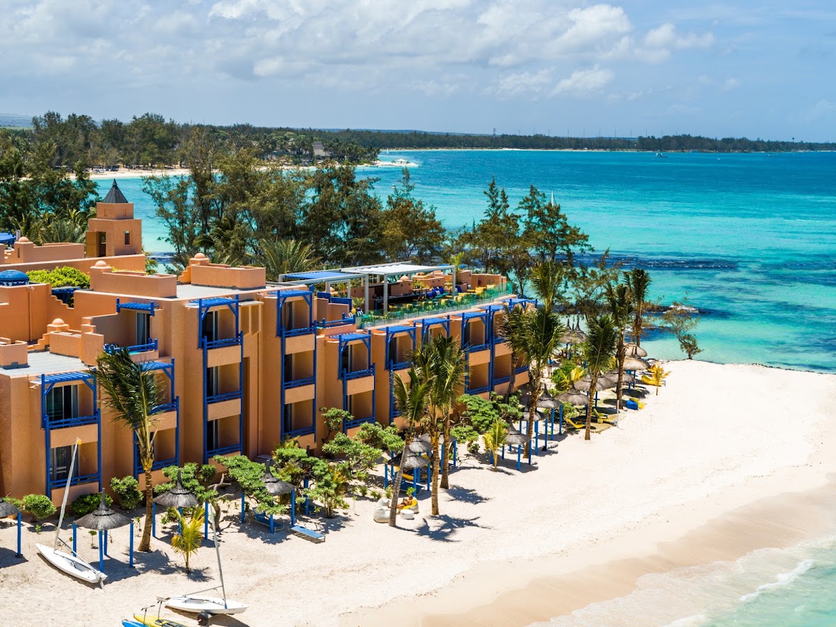 Terracotta buildings with blue accents line a white sand beach facing turquoise lagoon waters at SALT of Palmar.