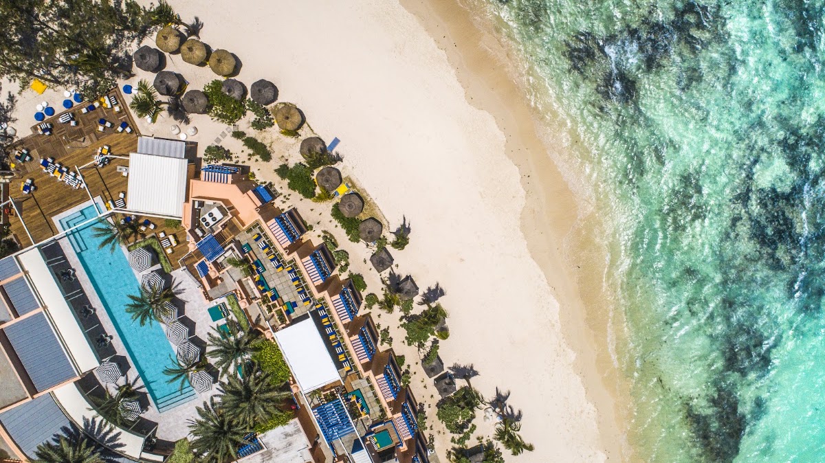 Aerial view of SALT of Palmar with blue pool, palm trees, thatched umbrellas, and turquoise ocean waters meeting sandy beach.
