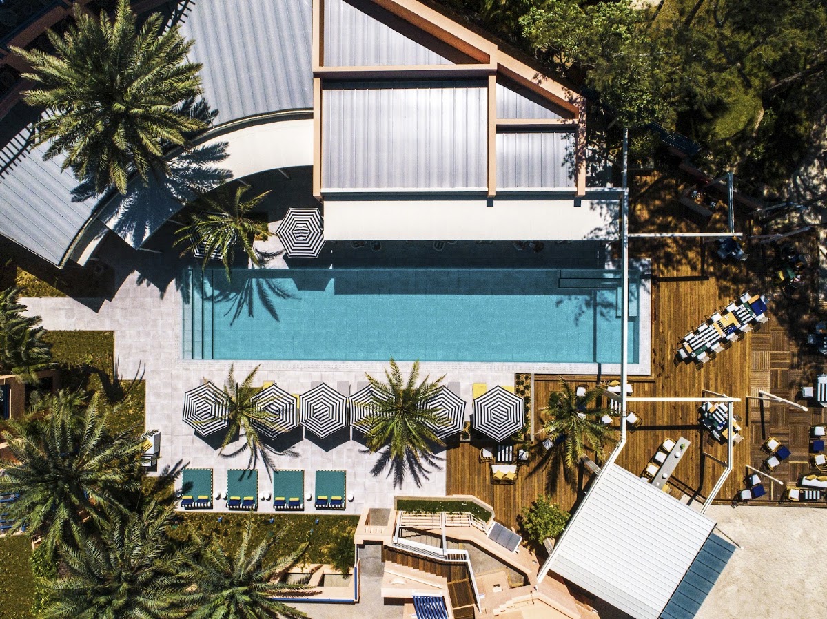 Overhead view of SALT of Palmar's rectangular pool surrounded by striped umbrellas, loungers, and palm trees on the deck.