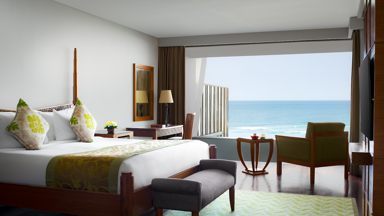 Spacious bedroom with king bed, teal accent stripe, geometric patterned accent wall, and floor-to-ceiling windows overlooking evening cityscape.