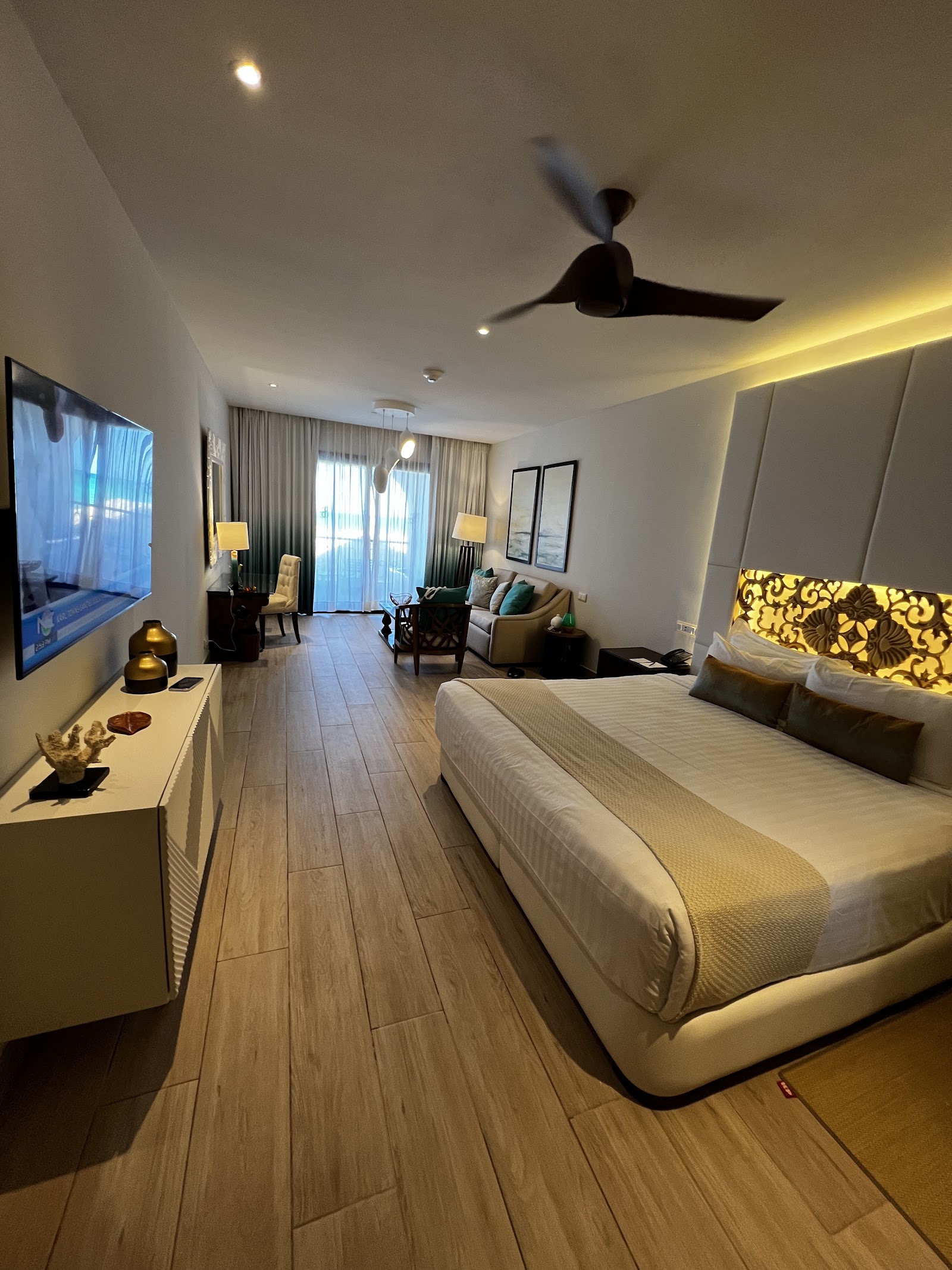 Spacious resort suite at Sanctuary Cap Cana with king bed, sitting area, flat-screen TV, and ocean-view balcony accessed through sheer curtains.