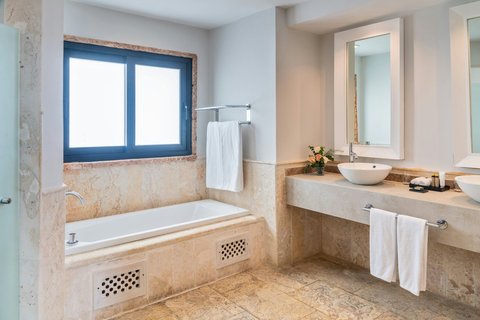 Bathroom with marble accents, sunken bathtub beneath blue-framed window, and vessel sink vanity at Sanctuary Cap Cana.