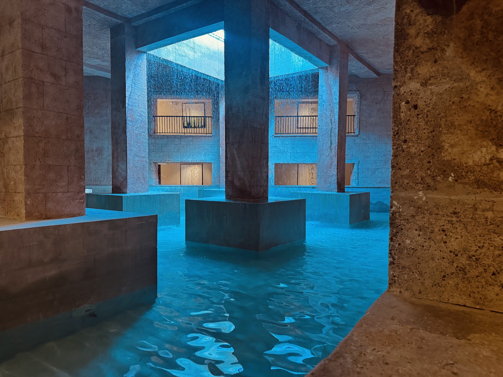 Underground pool at Sanctuary Cap Cana lit in bright blue with concrete pillars and walls, showing water features and architectural columns.