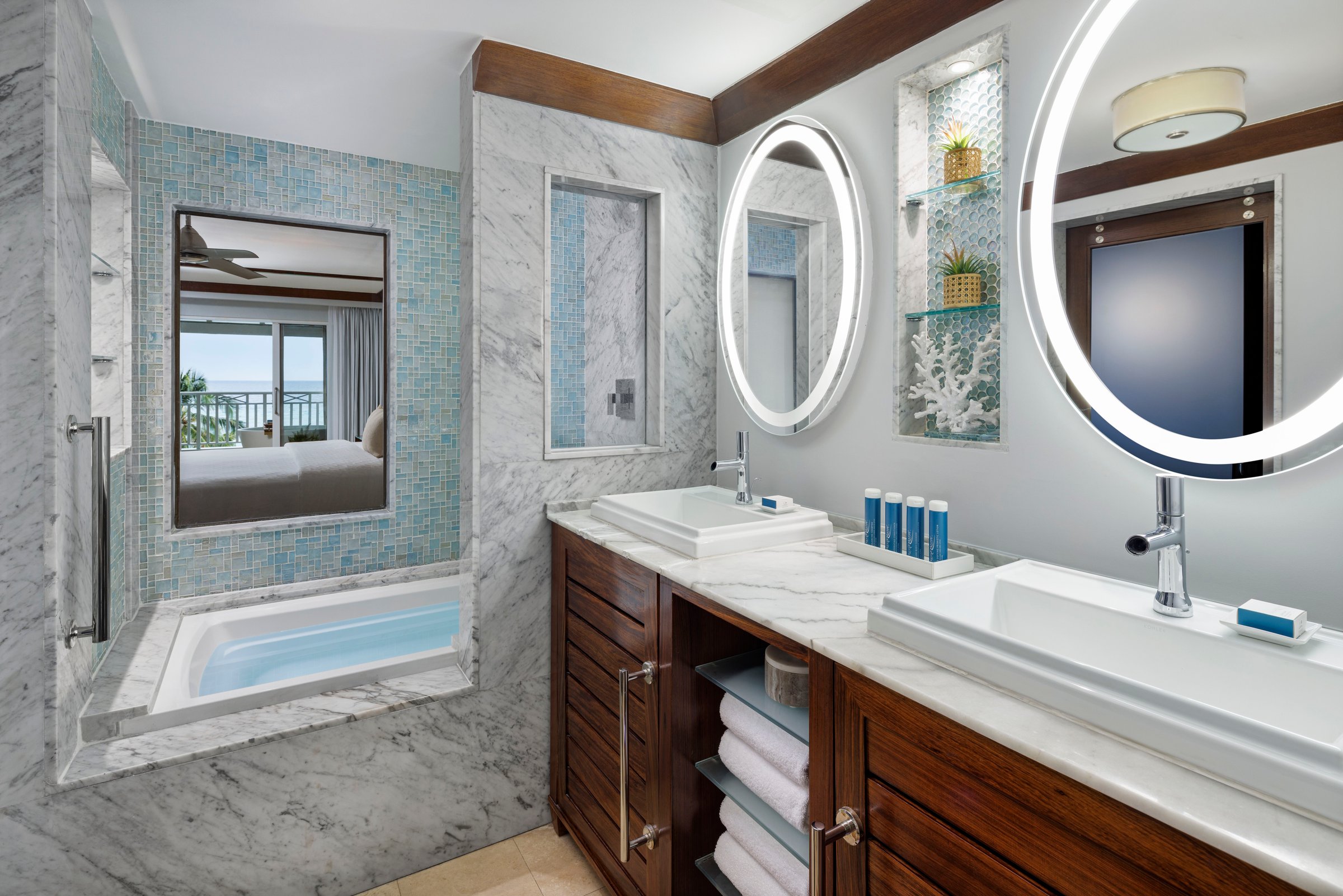 Marble bathroom with double sinks, round mirrors and a window tub.