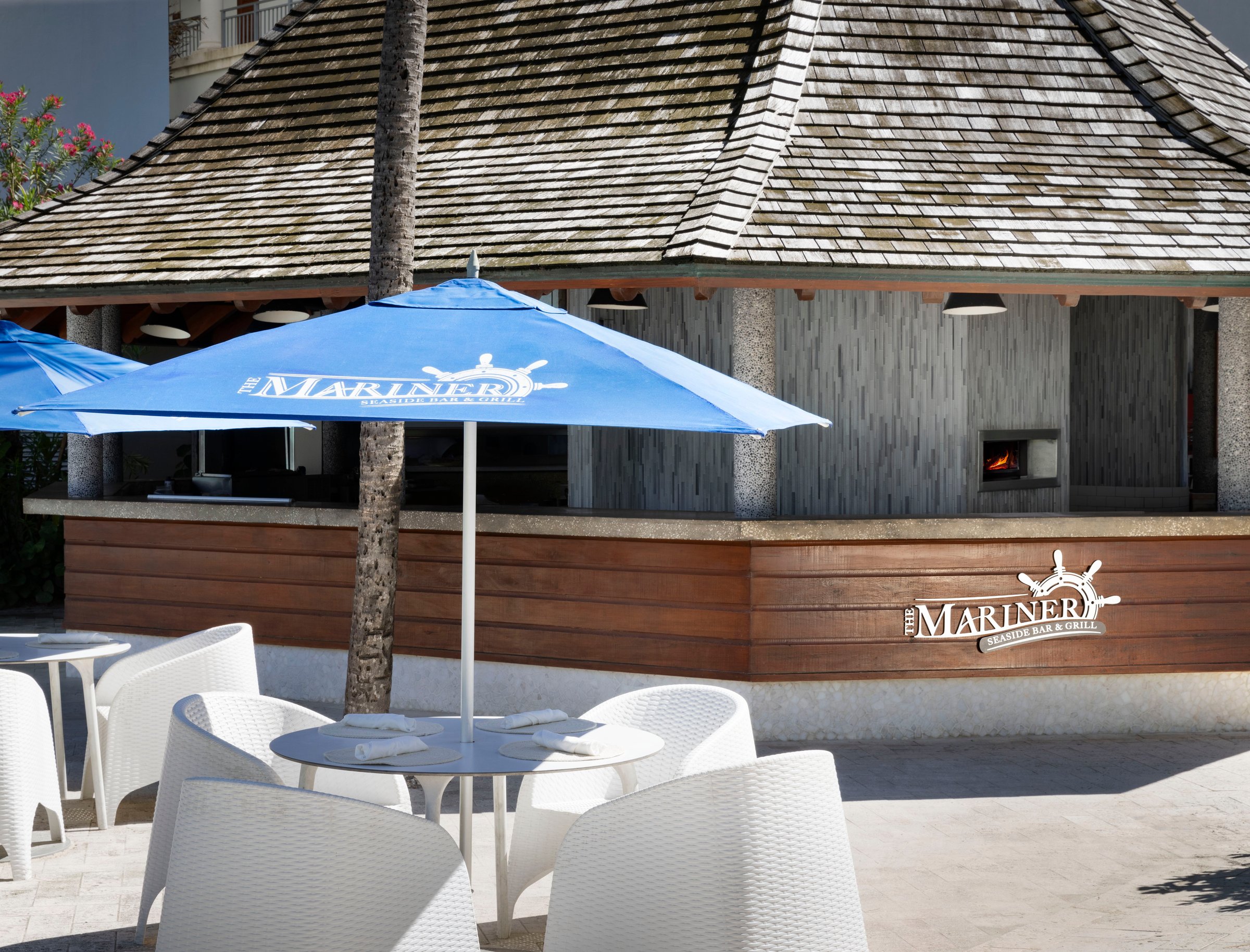 Mariners beach bar-restaurant with white chairs under a blue umbrella.