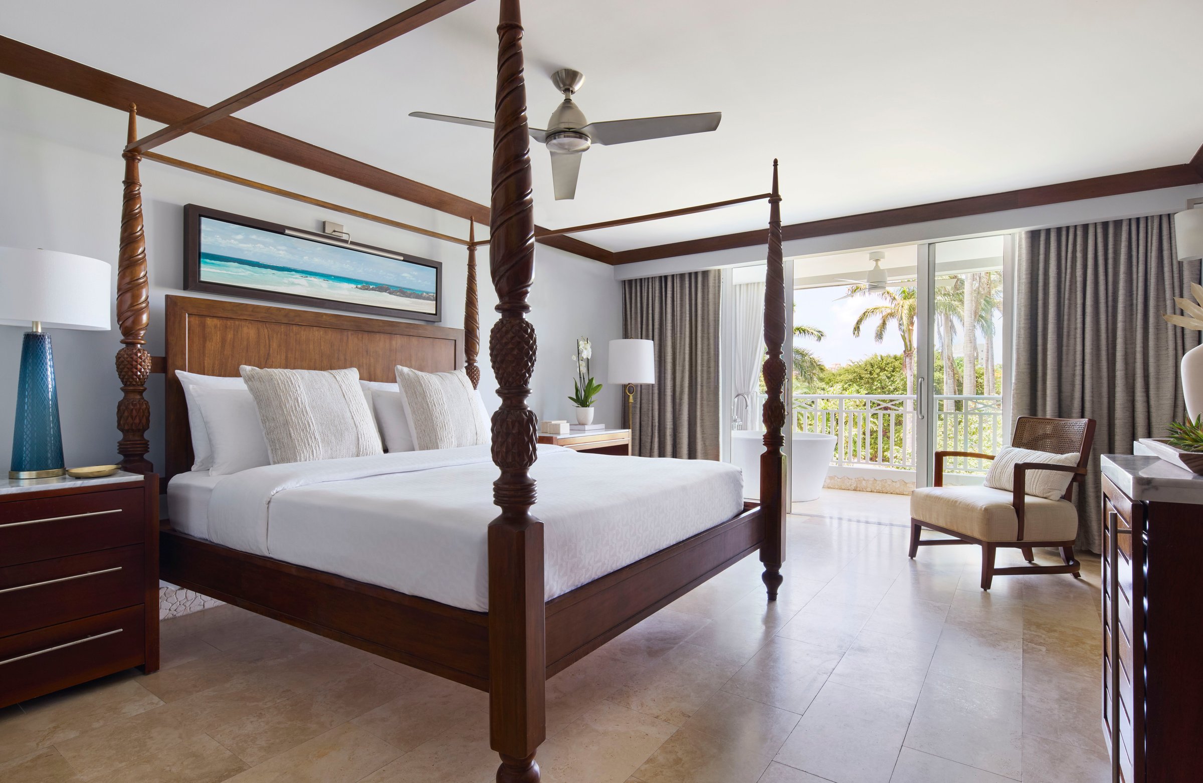 Four-poster bed in a bright suite with balcony doors and garden views.