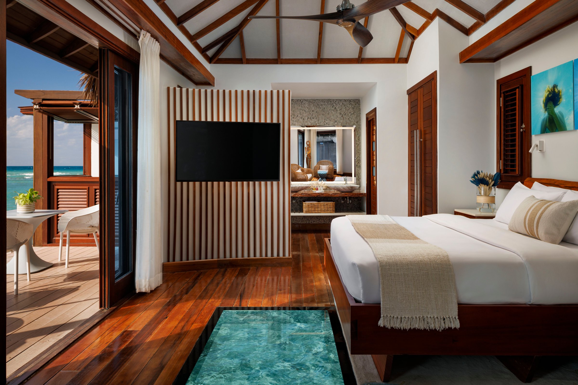 Over-water bungalow bedroom with glass floor panel and wood ceilings.
