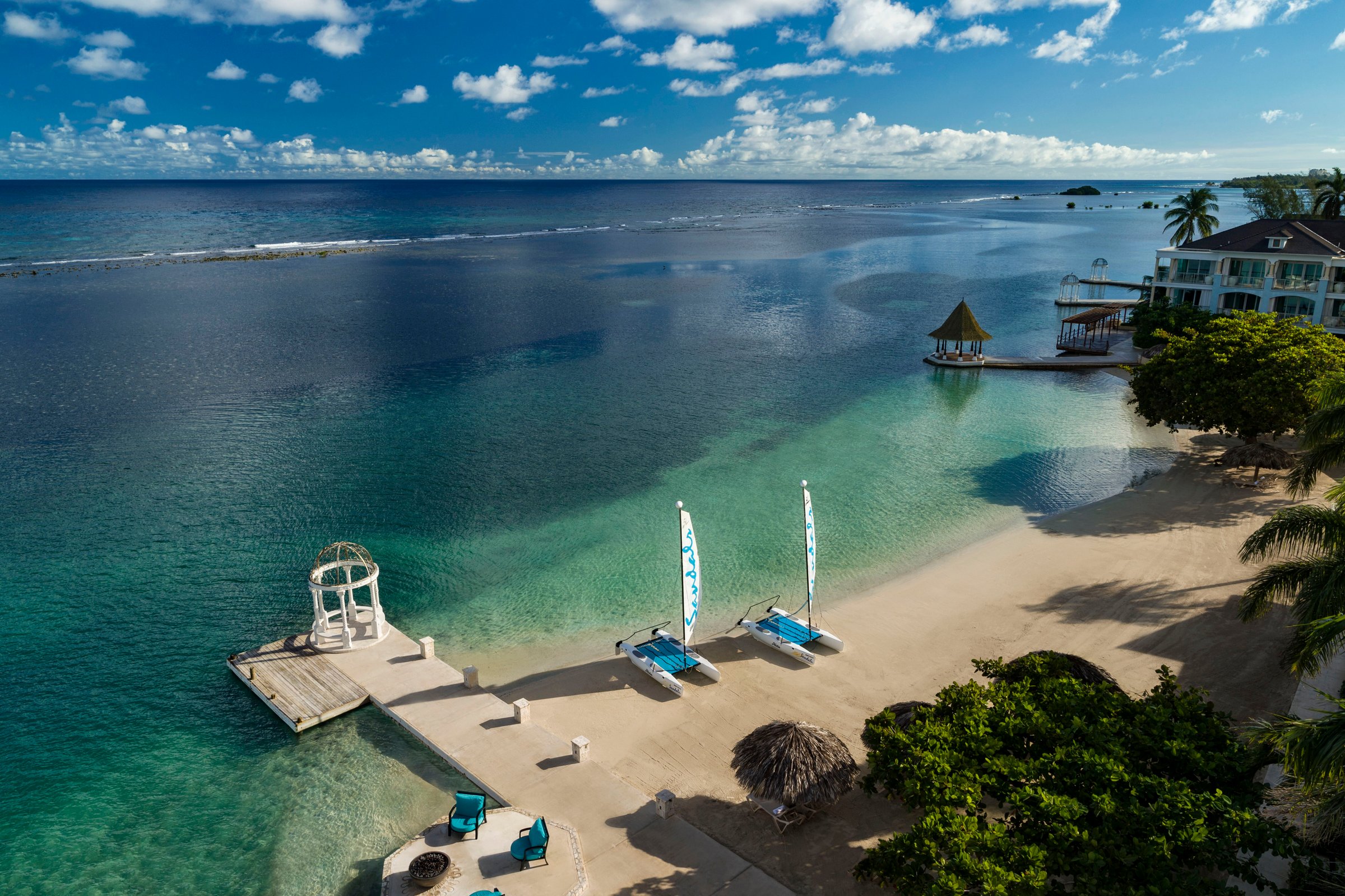 Aerial of the beach, pier and catamarans on turquoise water.