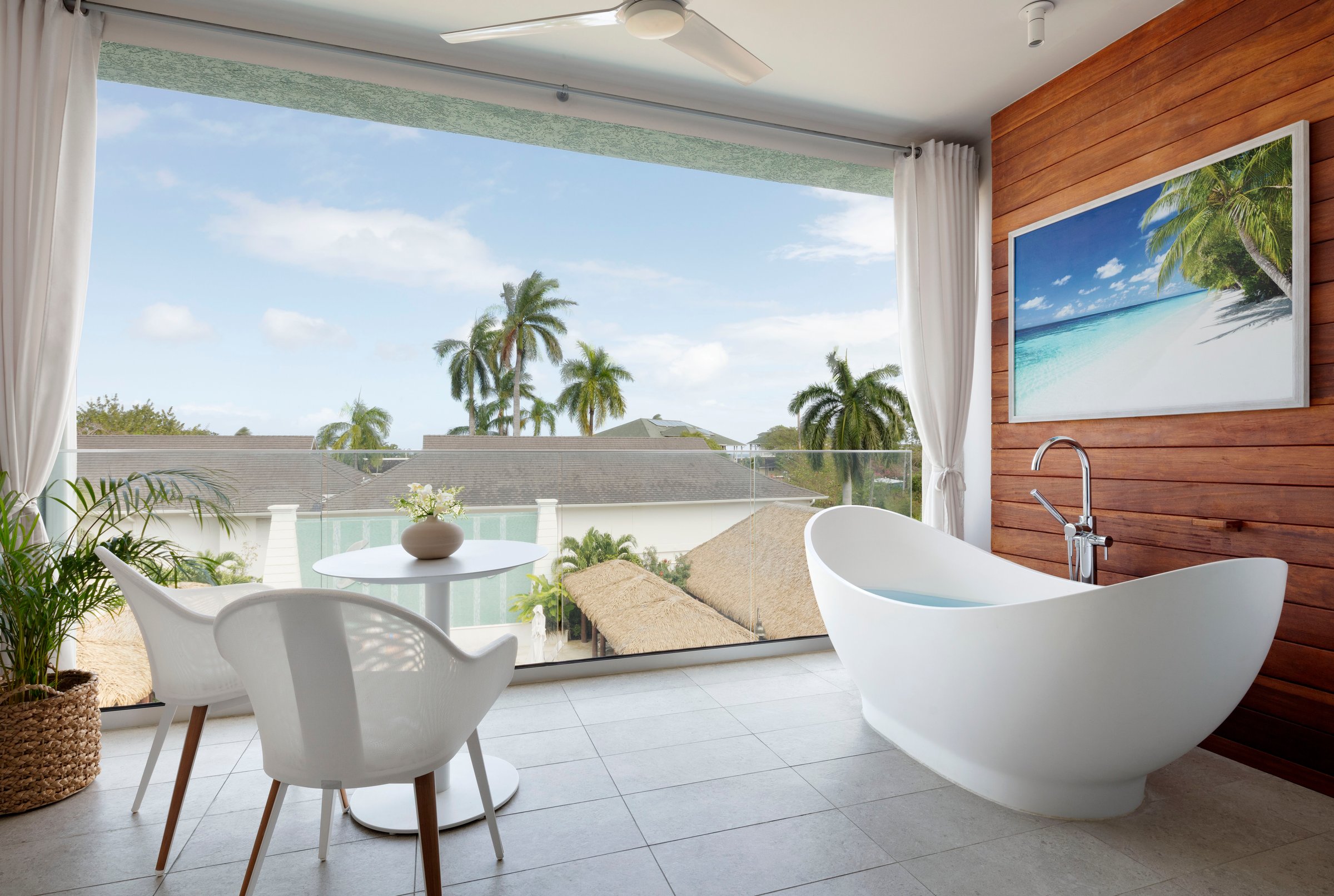 Suite with freestanding tub opening onto a balcony with palm views.
