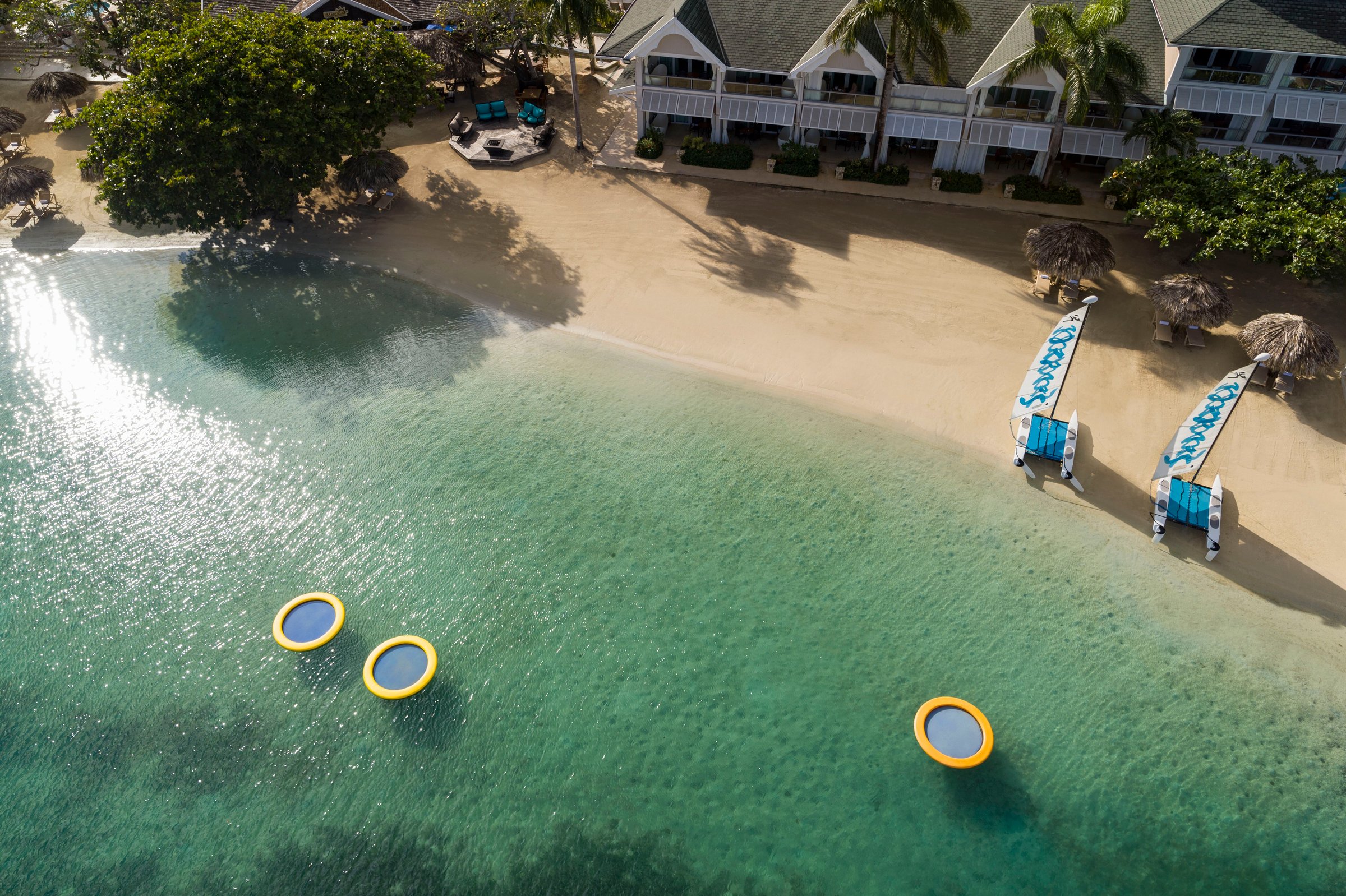 Overhead aerial of the beach cove with floats, loungers and clear shallows.