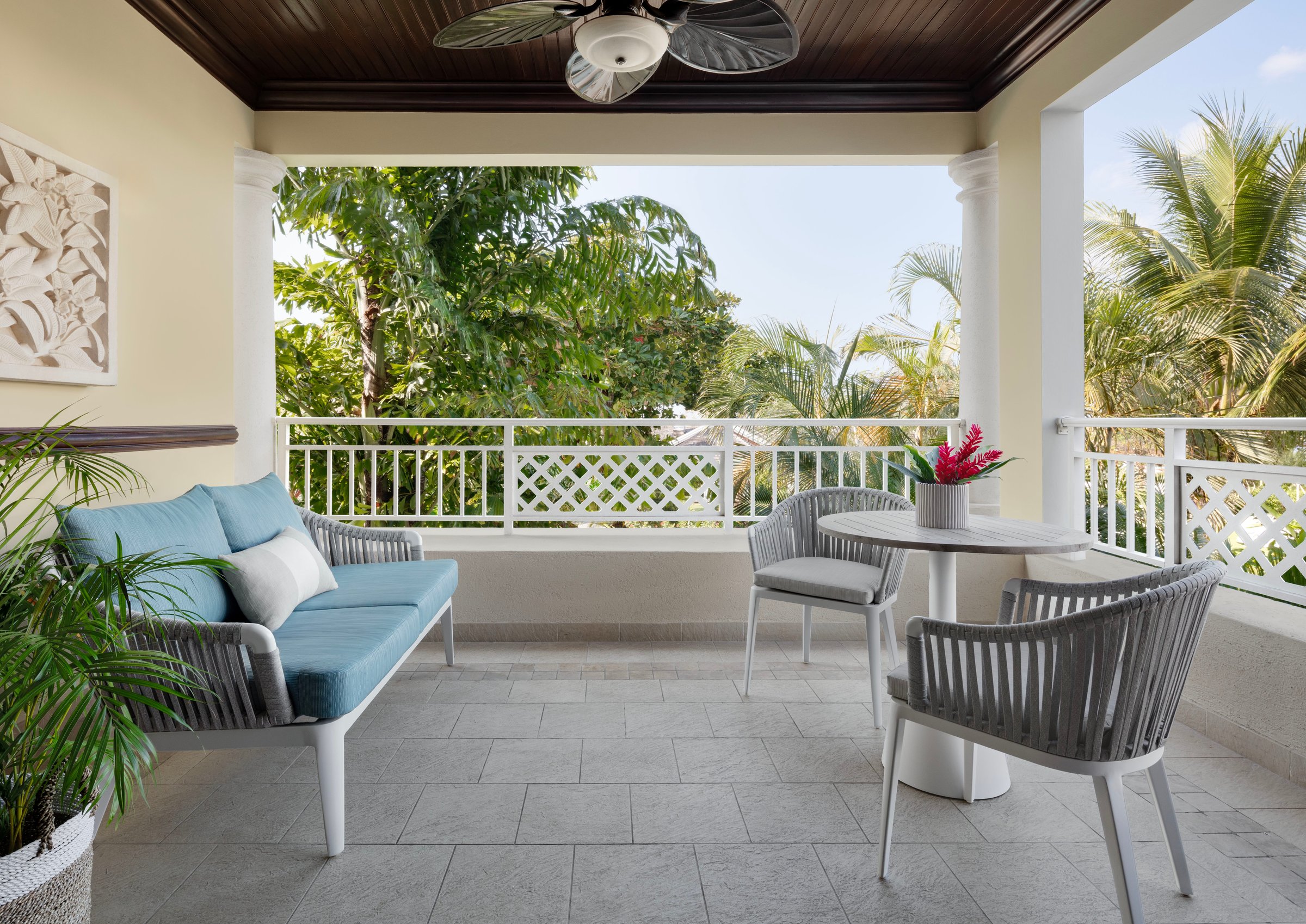 Covered balcony with sofa, bistro table and garden views.