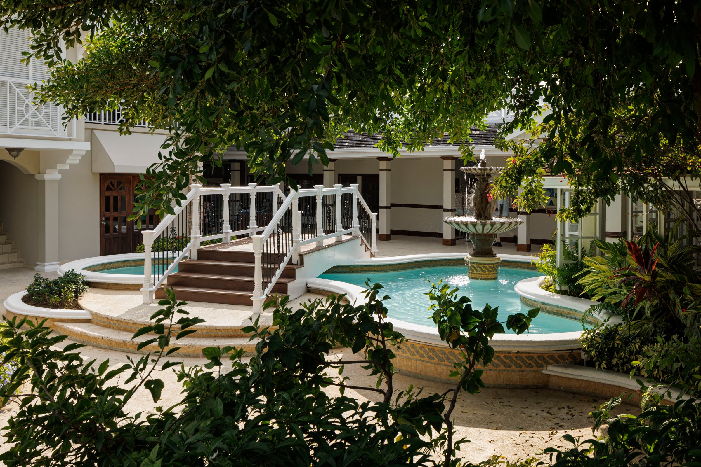 Courtyard fountain pool with white footbridge steps under shady trees.