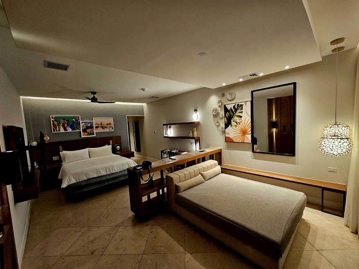 Spacious resort suite with king bed, separate sitting area with sofa, tile flooring, and modern lighting throughout.