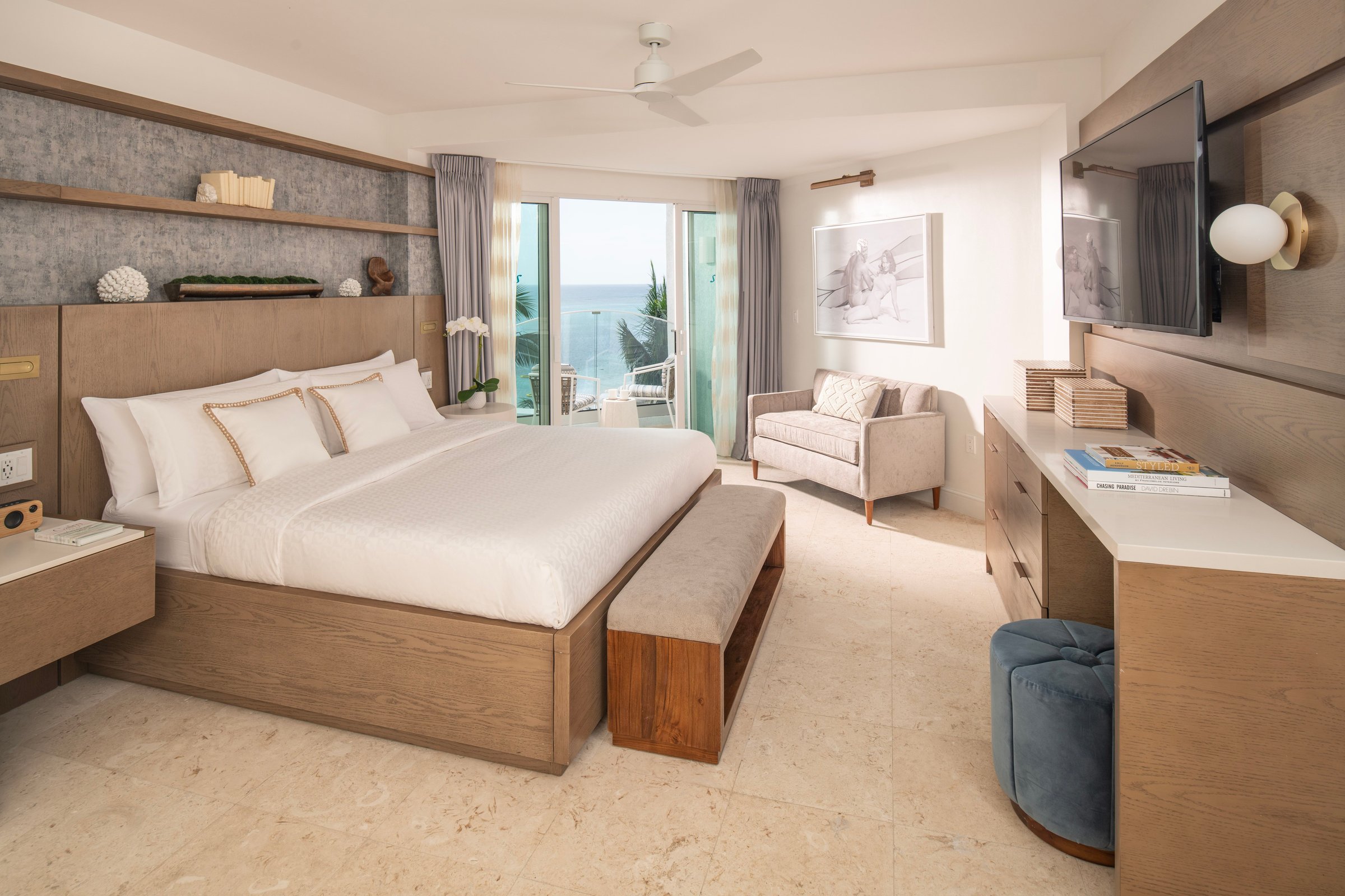 Bright bedroom with a white bed, stone floor and balcony doors to the sea.