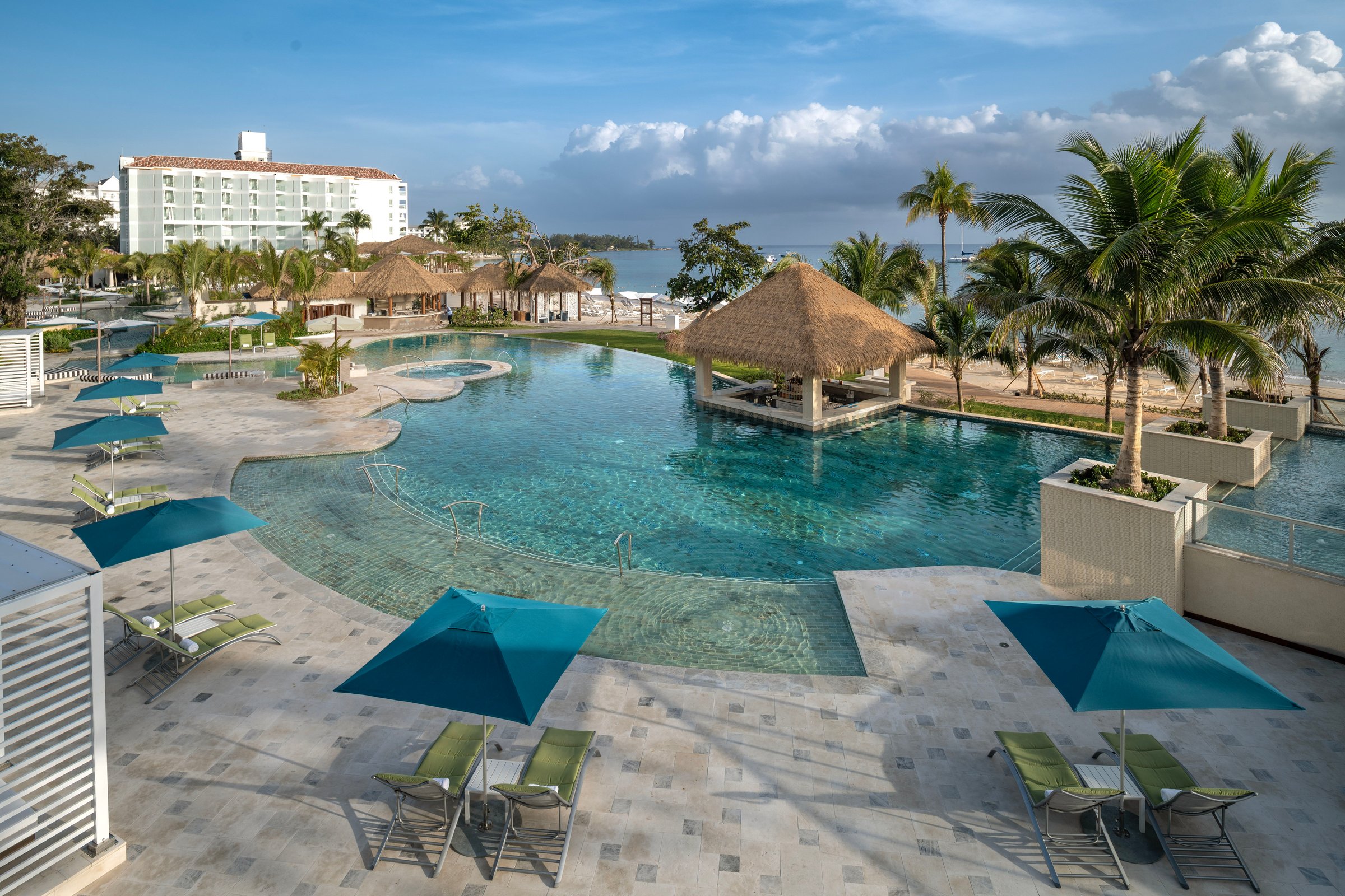 East pool with a thatched swim-up bar, teal umbrellas and the sea beyond.