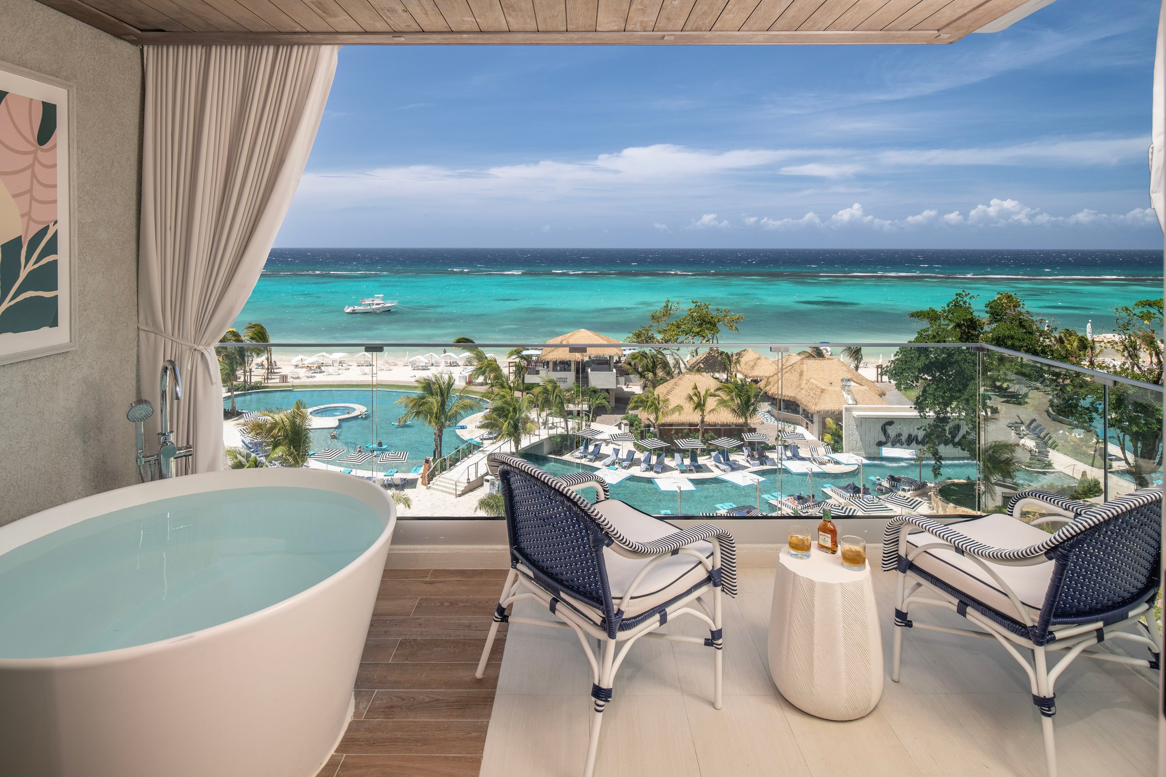 Balcony soaking tub and chairs overlooking the pools, beach and turquoise sea.