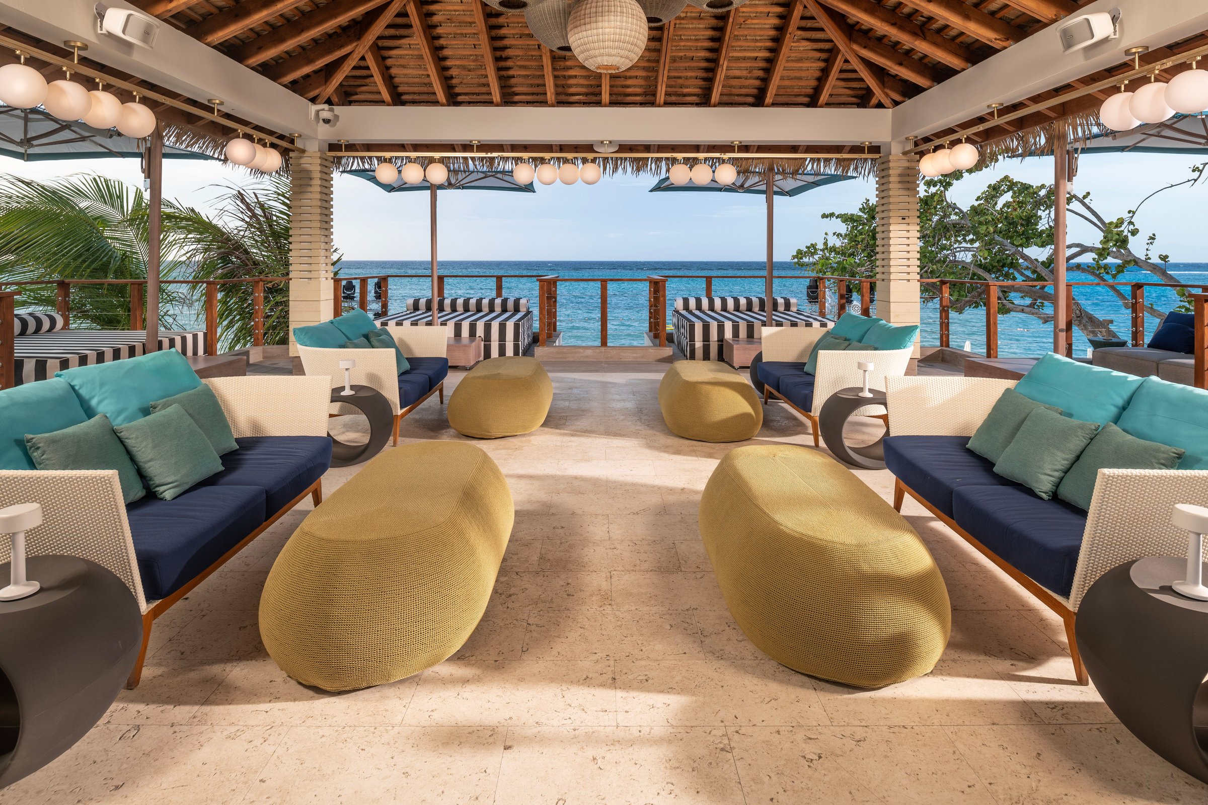 Open-sided seaside pavilion with navy-and-teal lounge seating and ocean views.