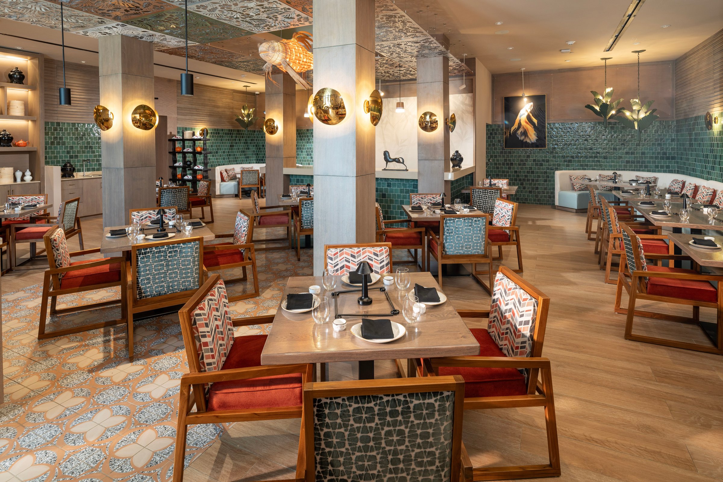 Banyu dining room with patterned chairs, green tile walls and brass lamps.