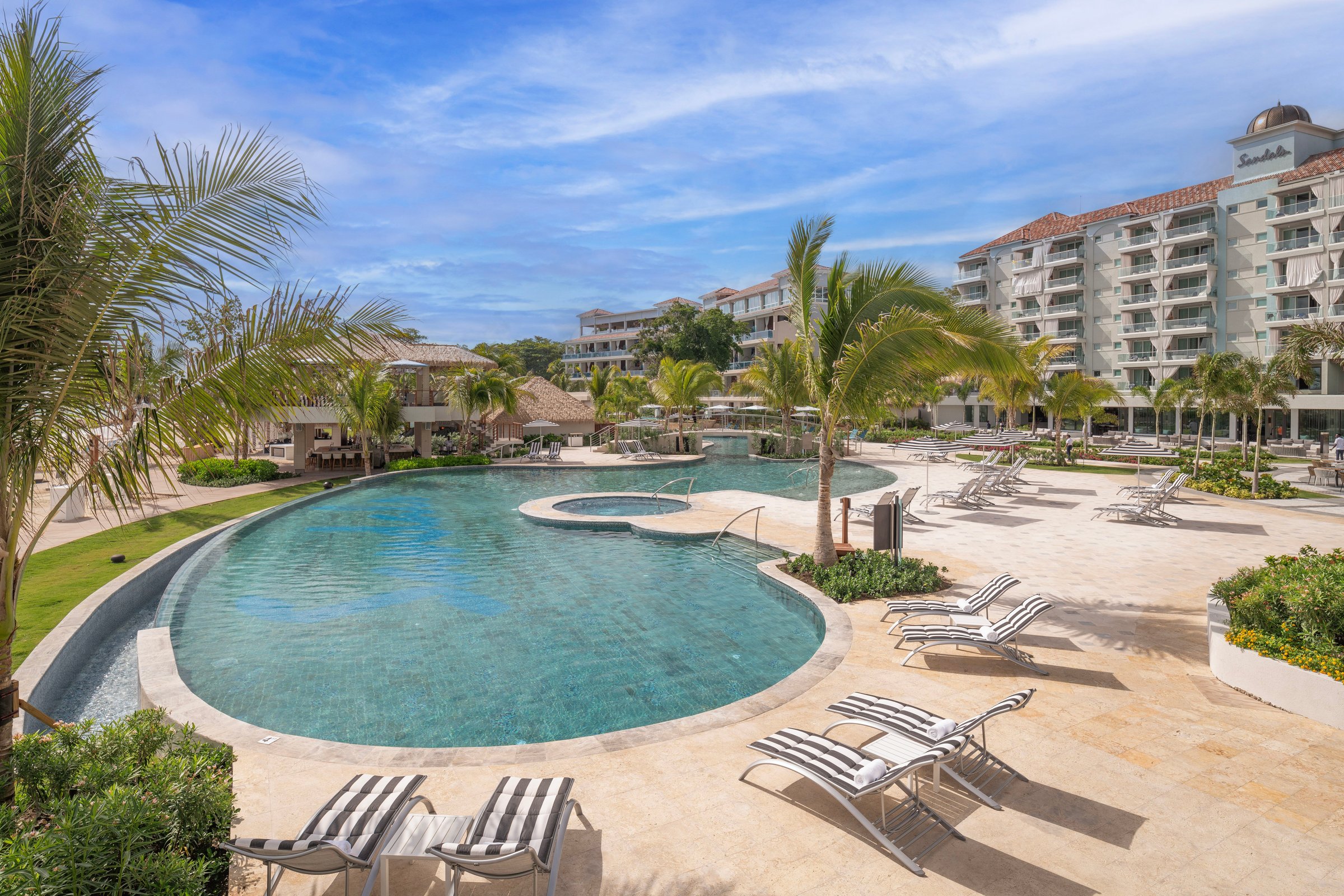 Curved West pool with striped loungers below the hotel wings.