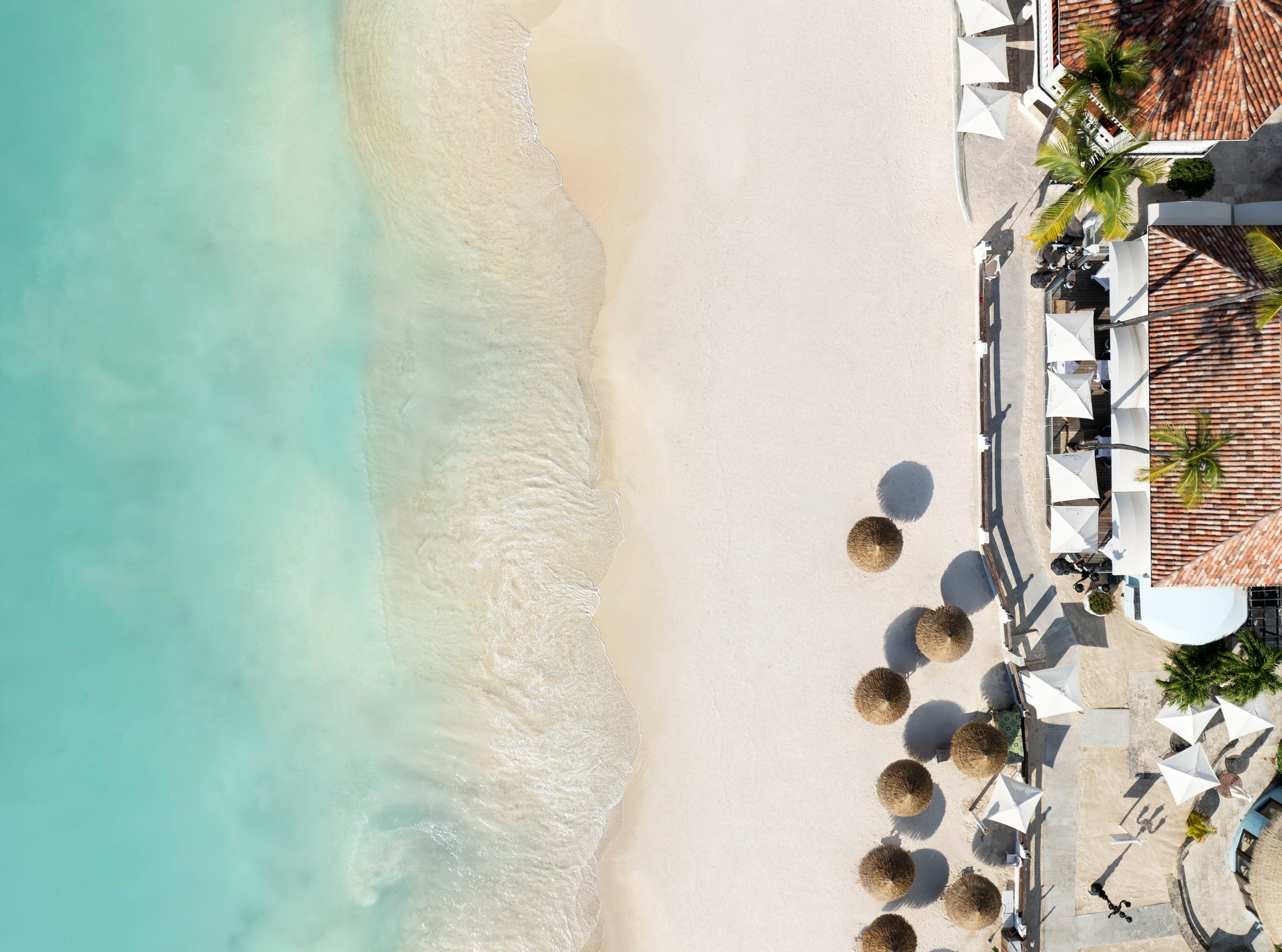 Top-down aerial of Dickenson Bay surf and sand beside Eleanor's beachfront terrace.