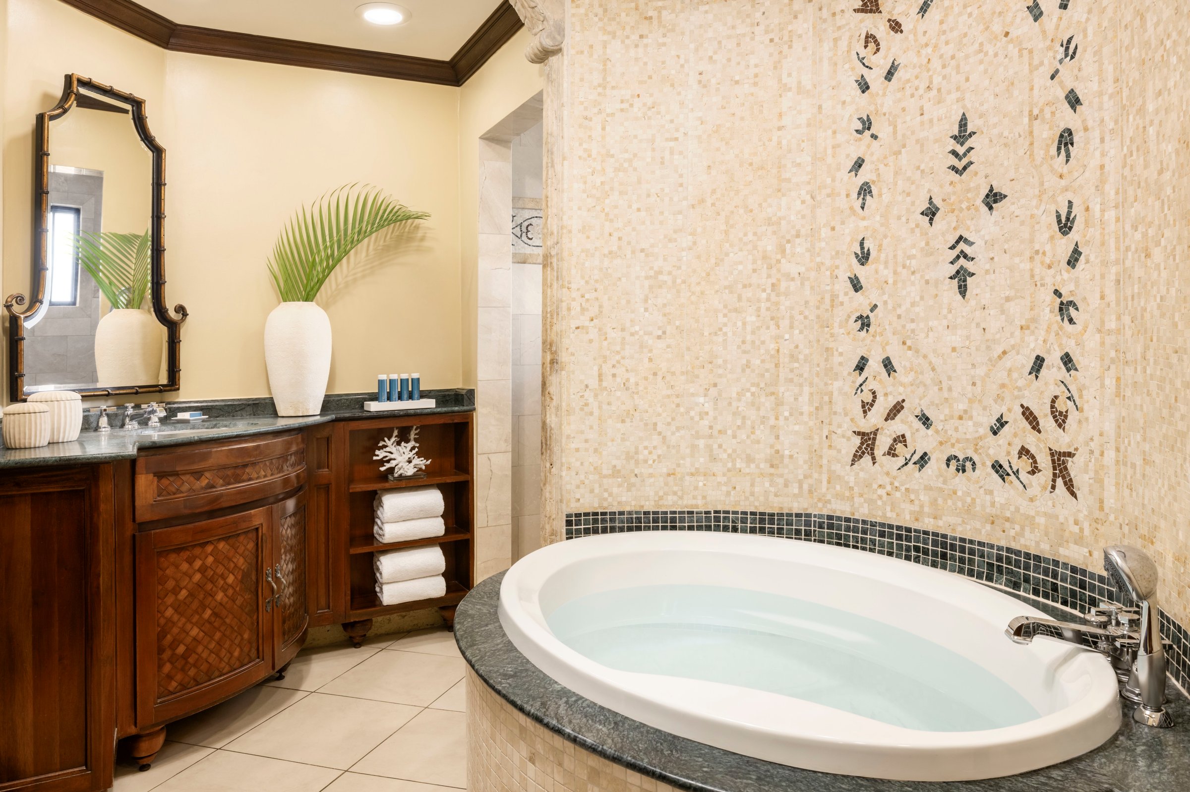 Suite bathroom with a soaking tub, mosaic wall and carved wood vanity.