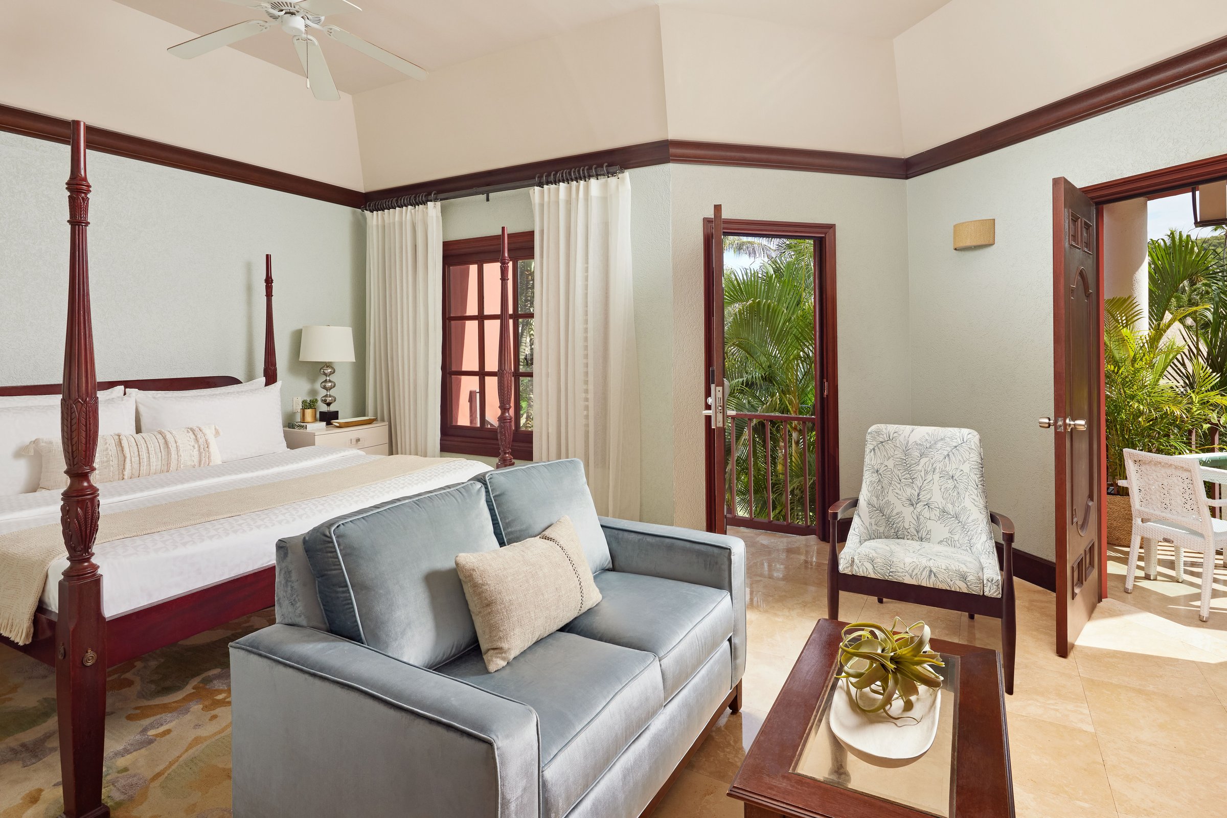 Suite bedroom with a four-poster bed, blue sofa and doors to a garden balcony.