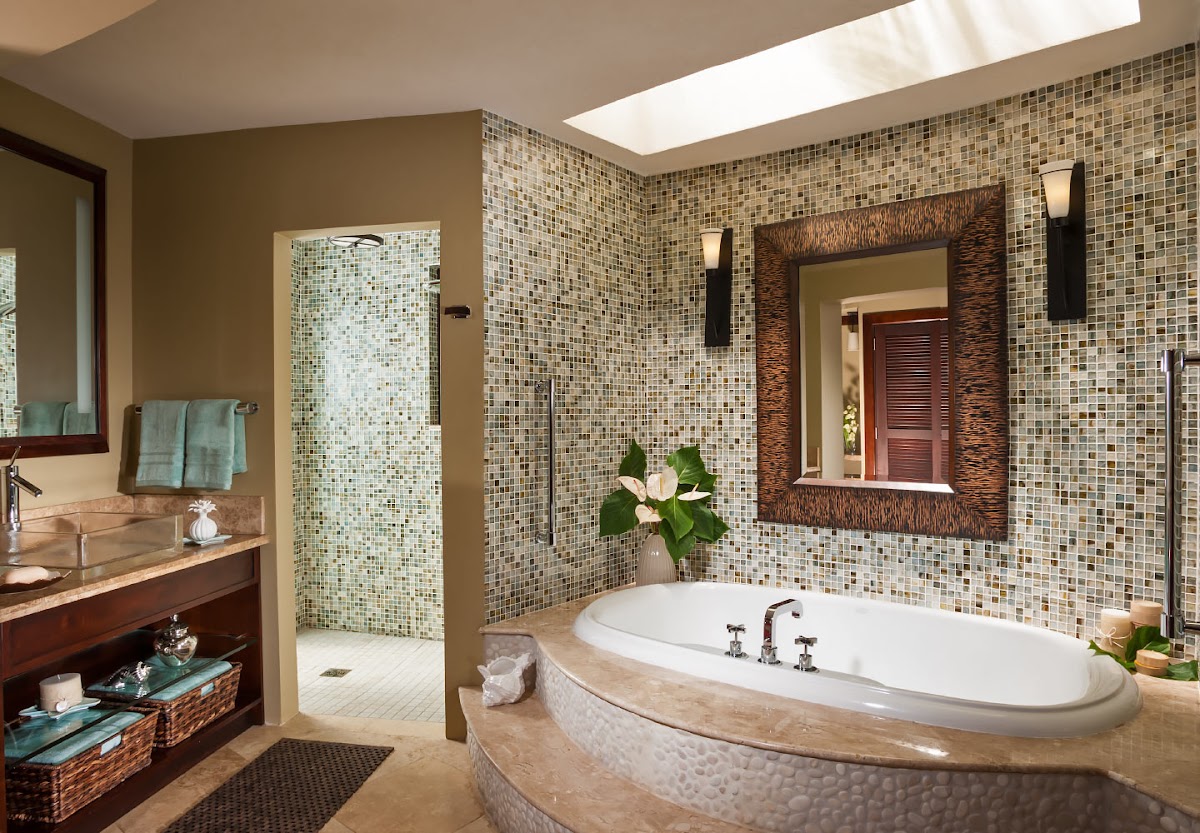 Luxury bathroom with sunken oval soaking tub, mosaic tile walls, glass-enclosed shower, dark wood vanity, and skylight at Sandals Grande St. Lucian.