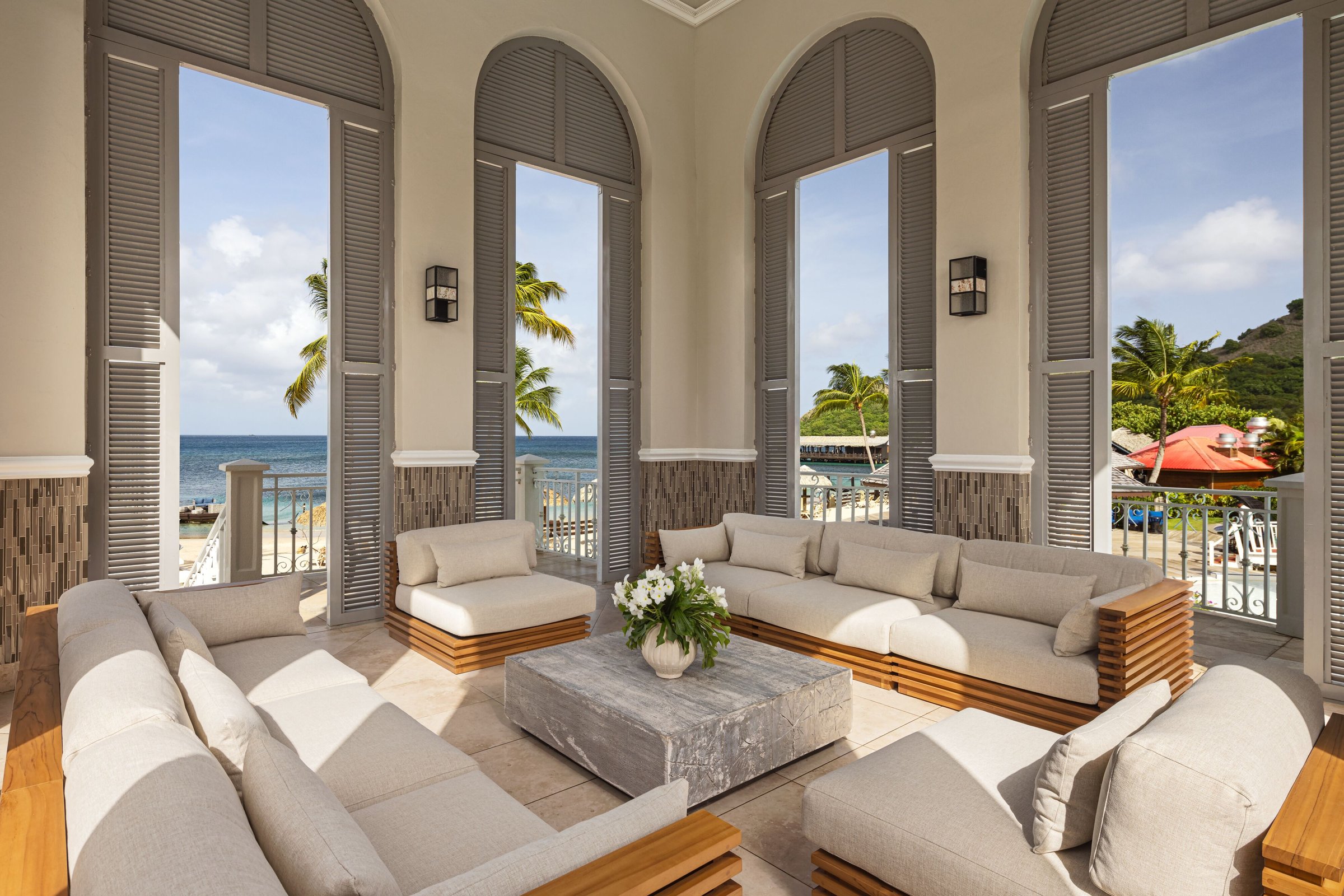 Arched poolside lounge with deep sofas and sea views through shutters.