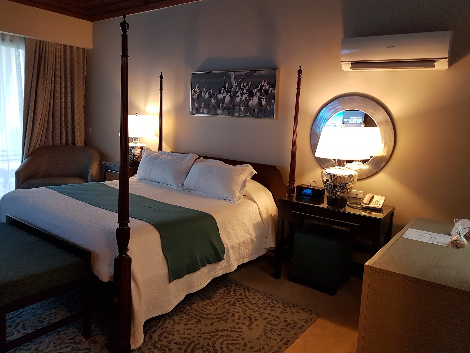 Resort guestroom with queen bed, white furnishings, ensuite bathroom visible through open door, and flat-screen TV on wall.