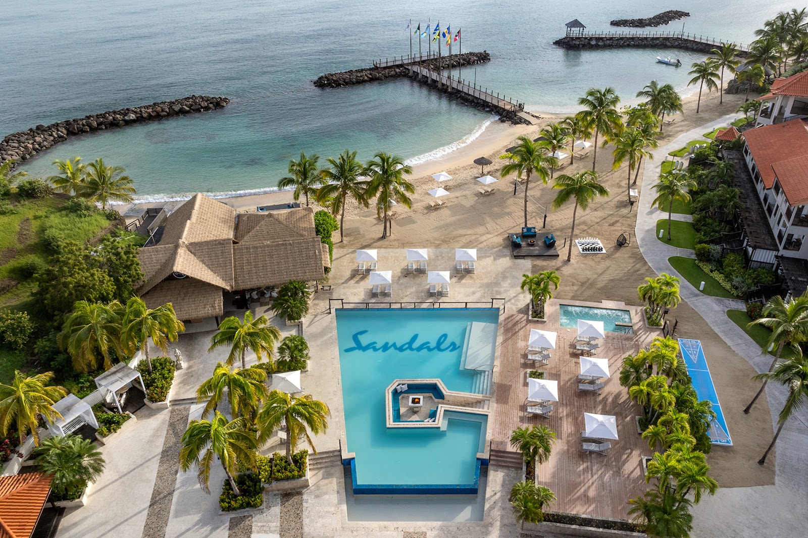 Sandals Grenada resort pool and beach with palm trees, lounge chairs, and rocky breakwater protecting the turquoise bay.