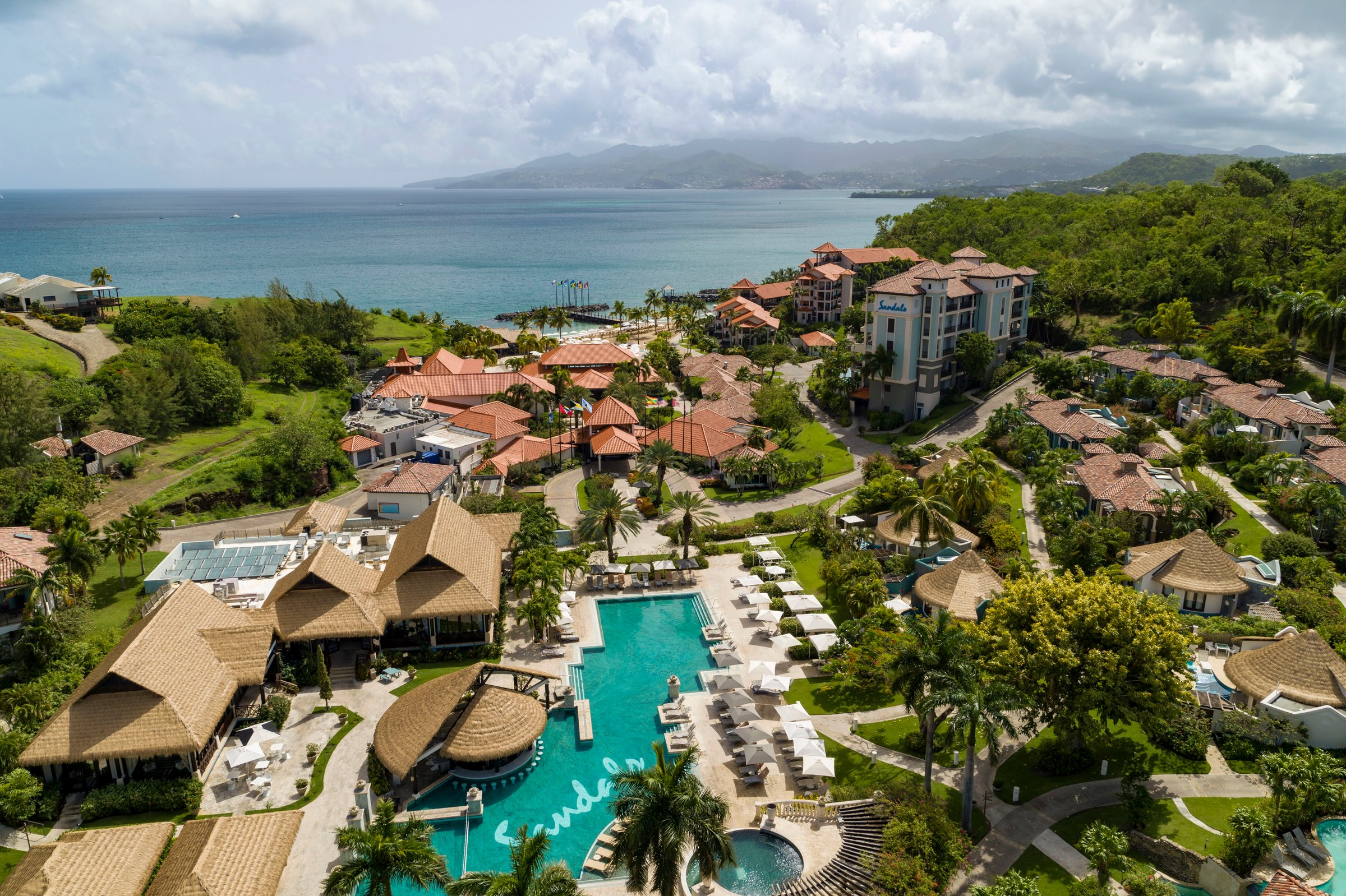 Aerial of the thatched pool courtyard, villas and gardens running to the sea.