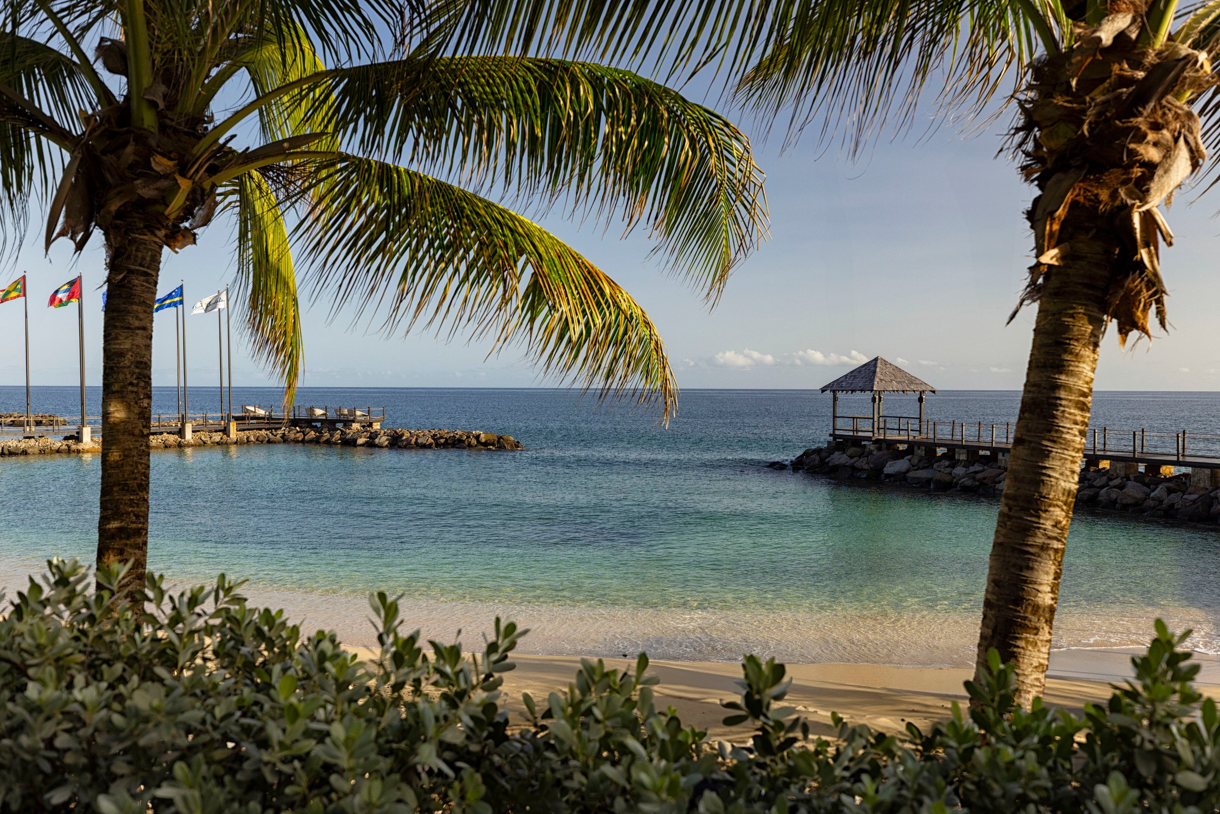 Calm bay between leaning palms with a gazebo pier on the breakwater.