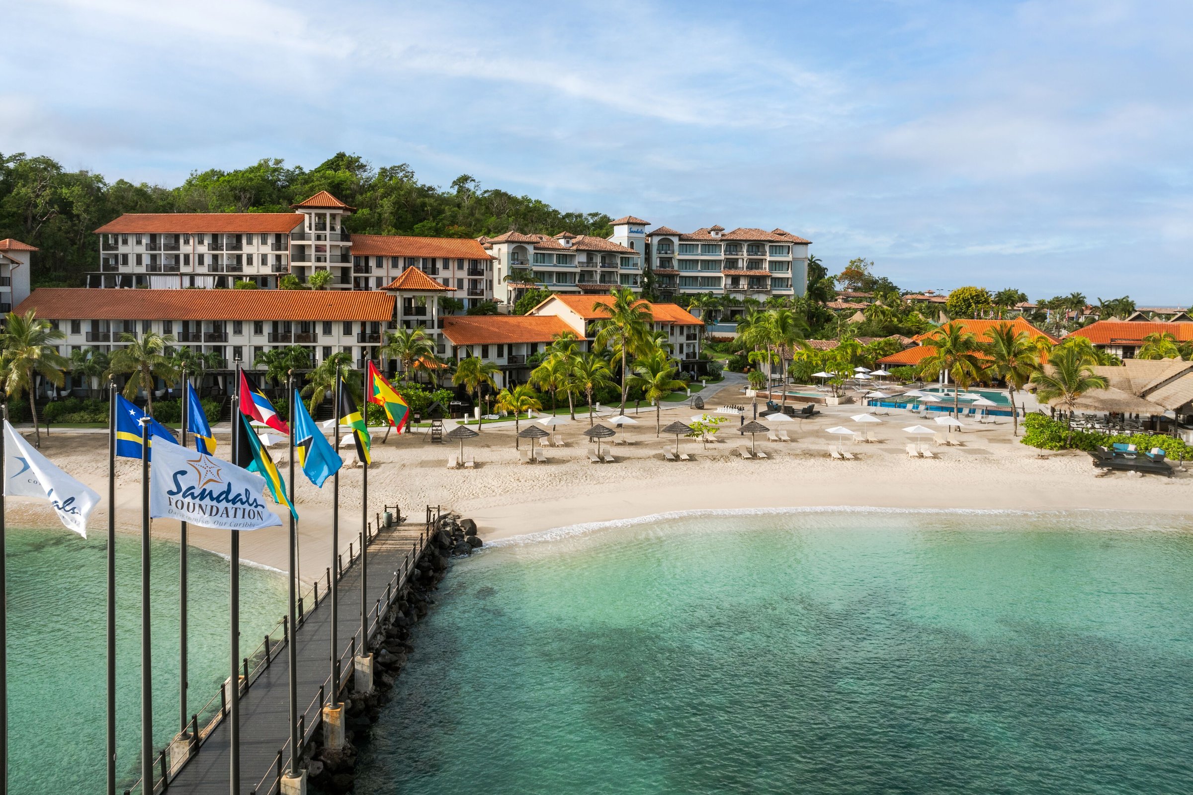 Flag-lined pier over turquoise water leading to Pink Gin Beach and the resort.