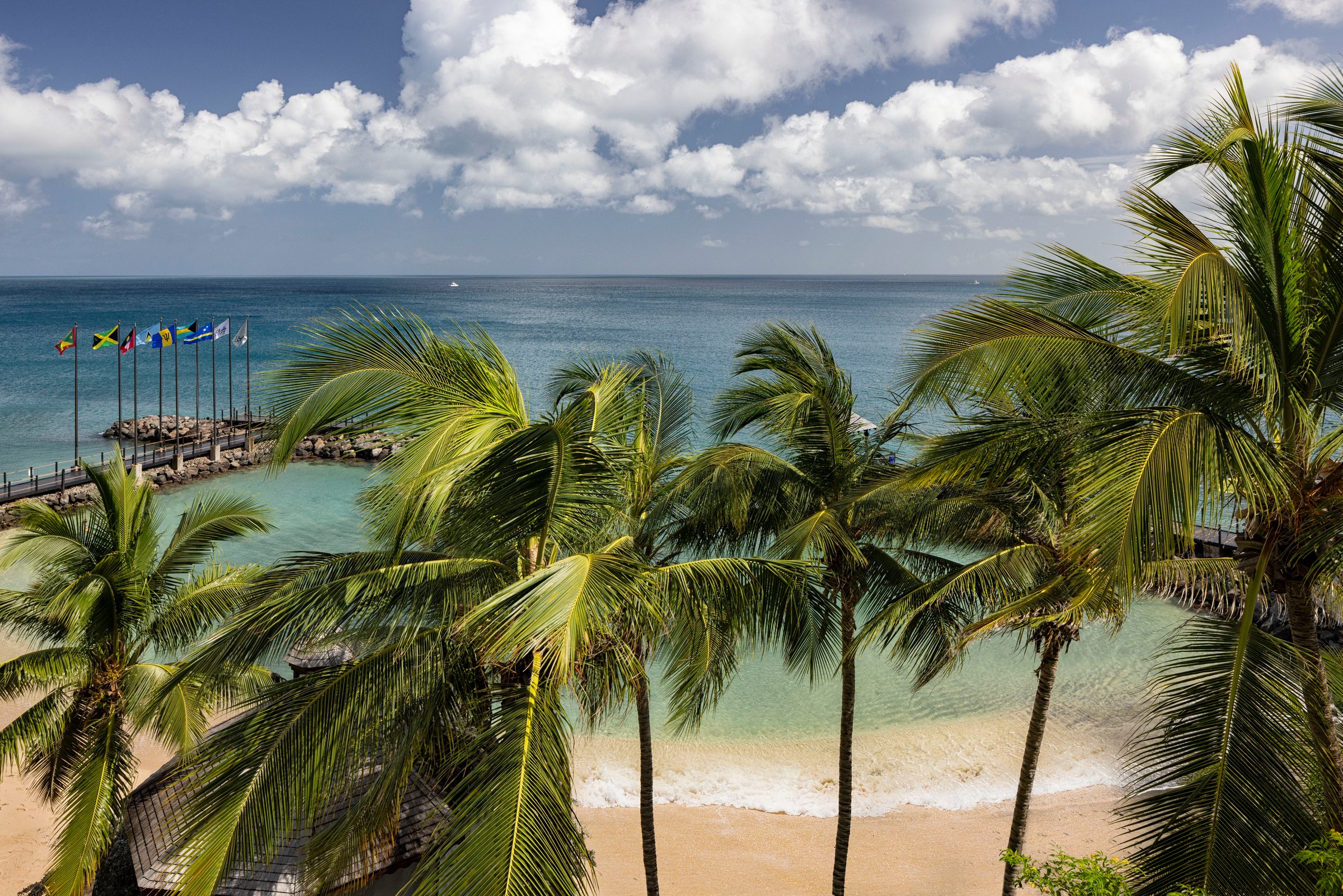 Palms framing a sheltered sandy cove with the flag pier and turquoise water.