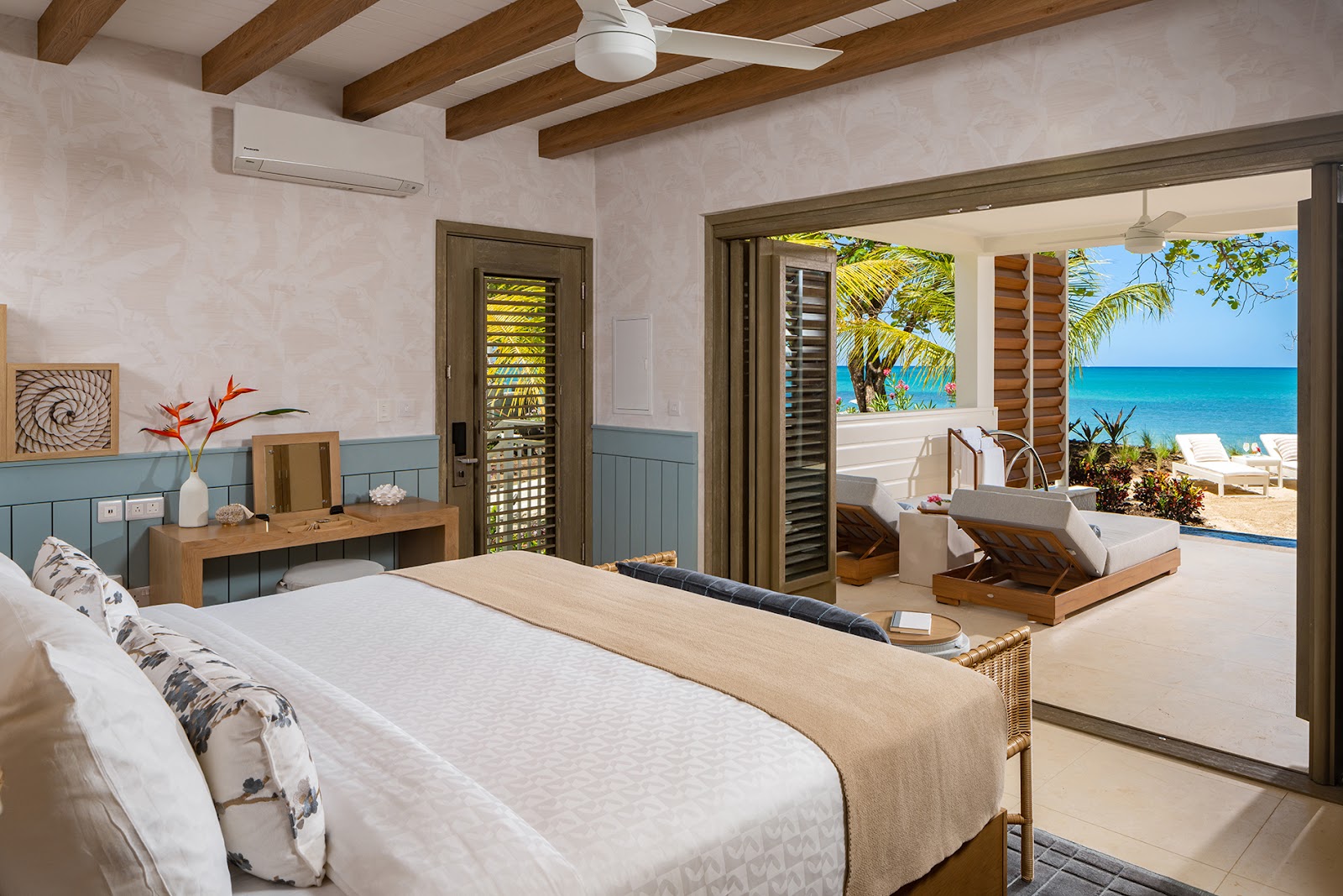 Beachfront room at Sandals Halcyon Beach with king bed, wooden beams, open doors to terrace with lounge chairs, ocean and palm trees visible.